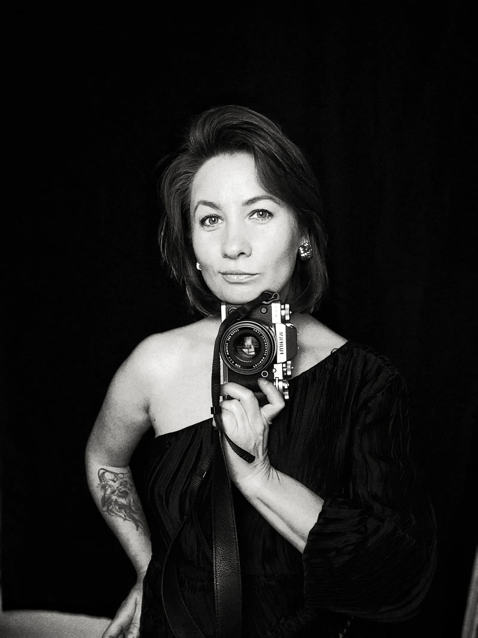 Irene Ardan, portrait photographer, holding her camera against a black backdrop