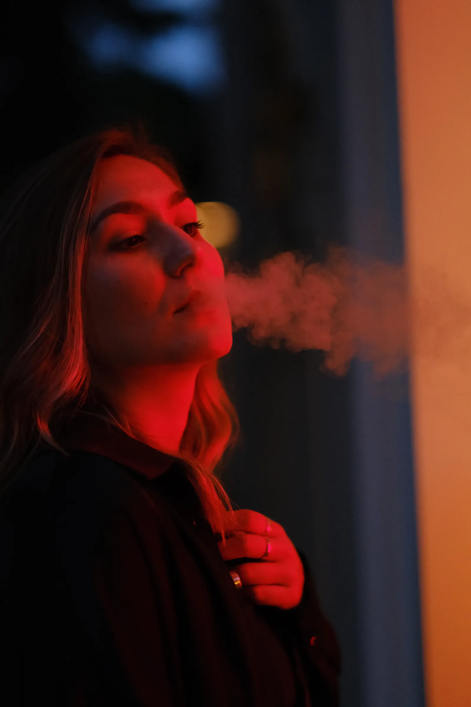 Woman in red light lying back and exhaling smoke against an evening sky
