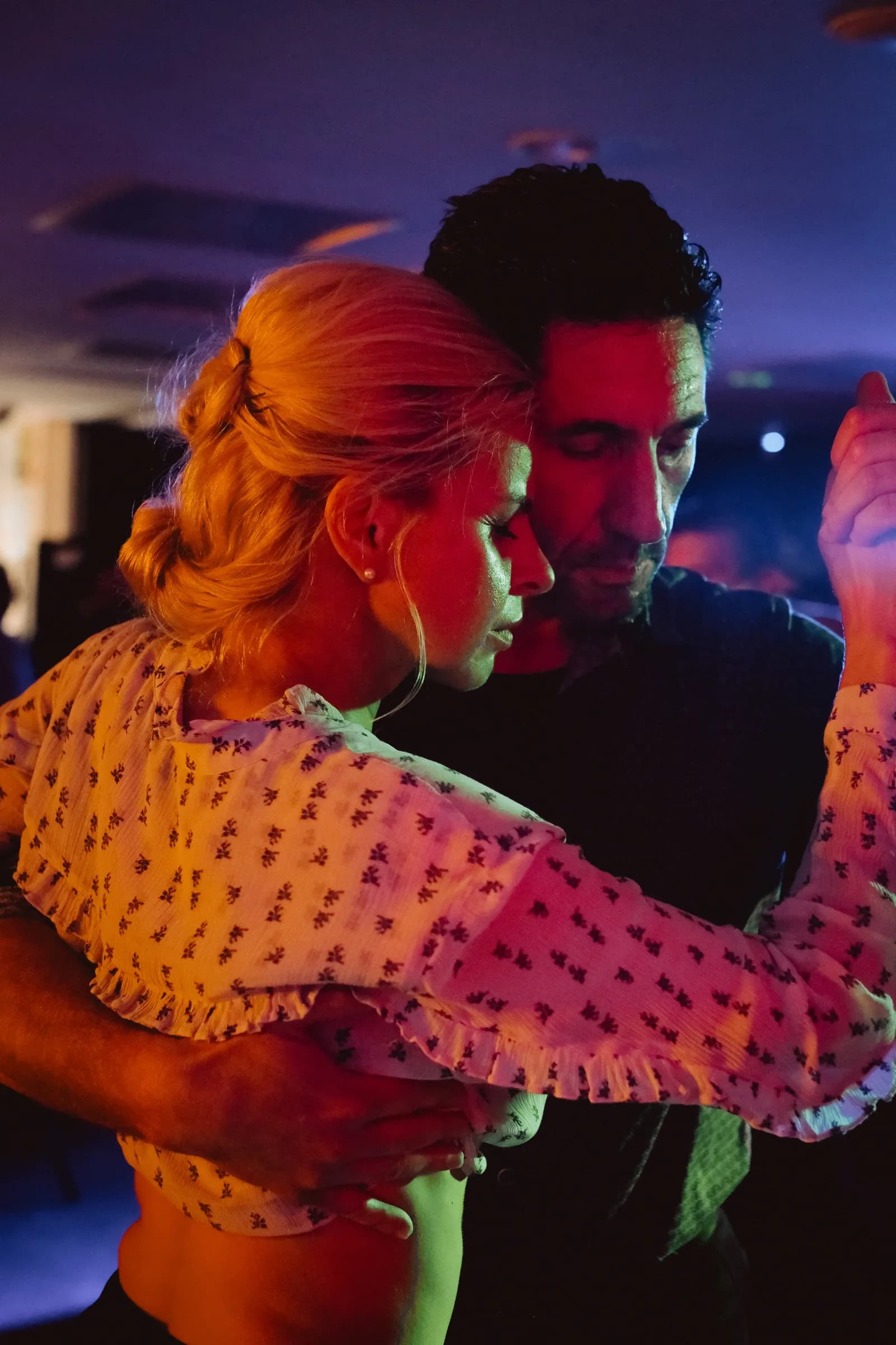 Blonde woman dancing forehead to forehead with her partner in violet and amber club light