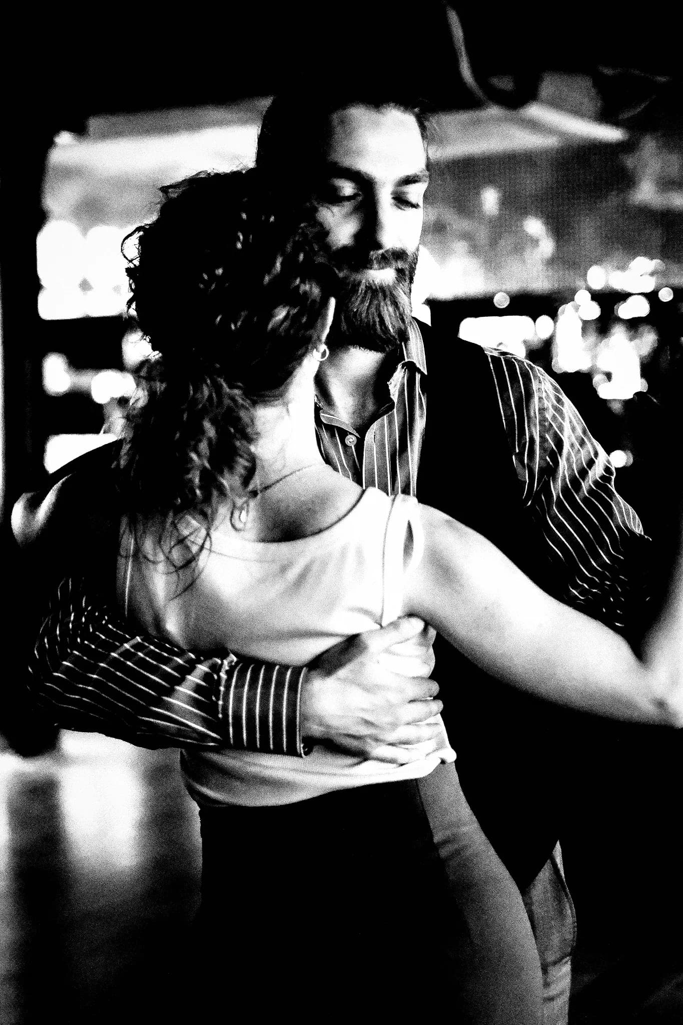 Bearded man in a striped shirt holding his partner close, seen over her shoulder
