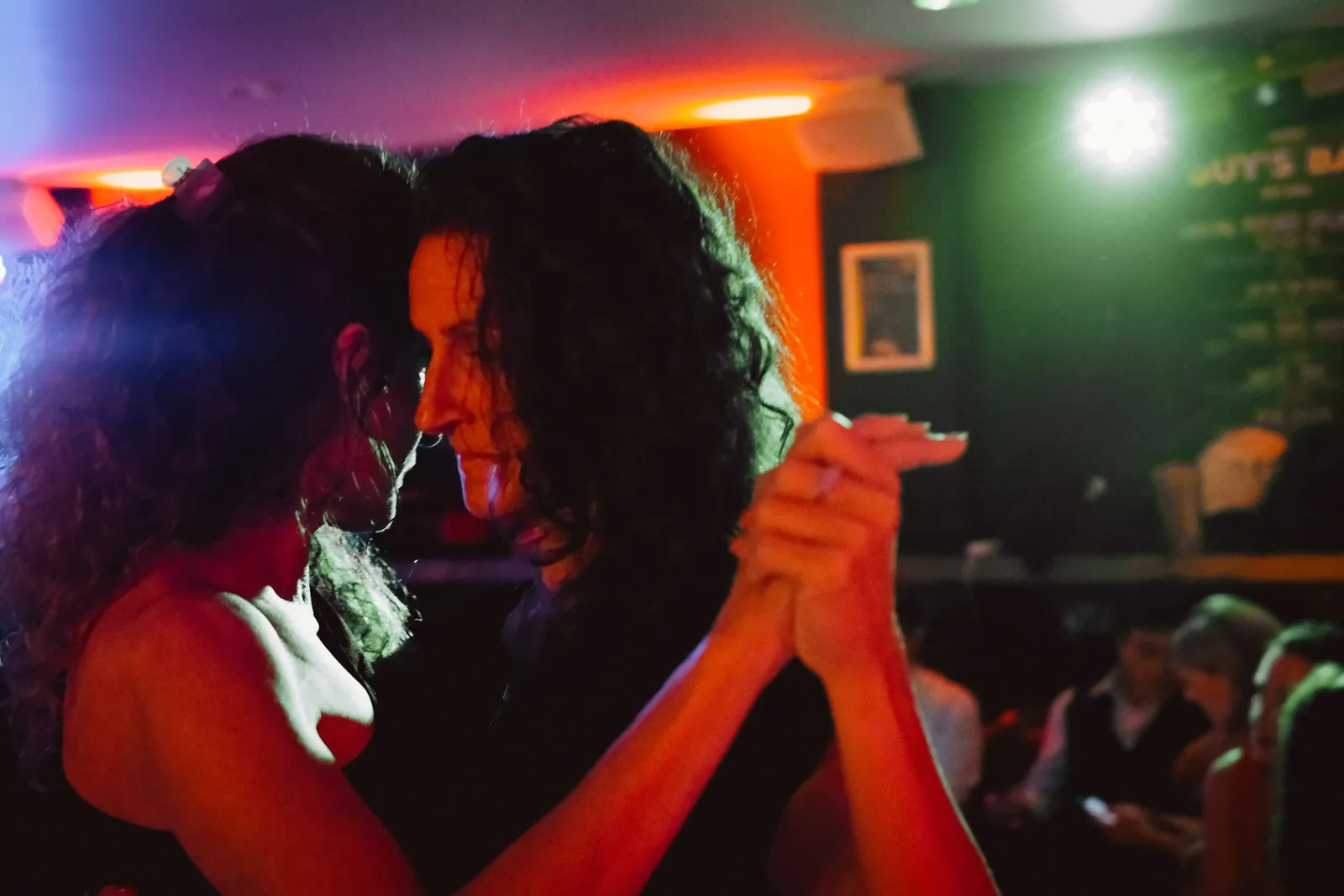 Two women dancing tango together in the orange light of a London bar