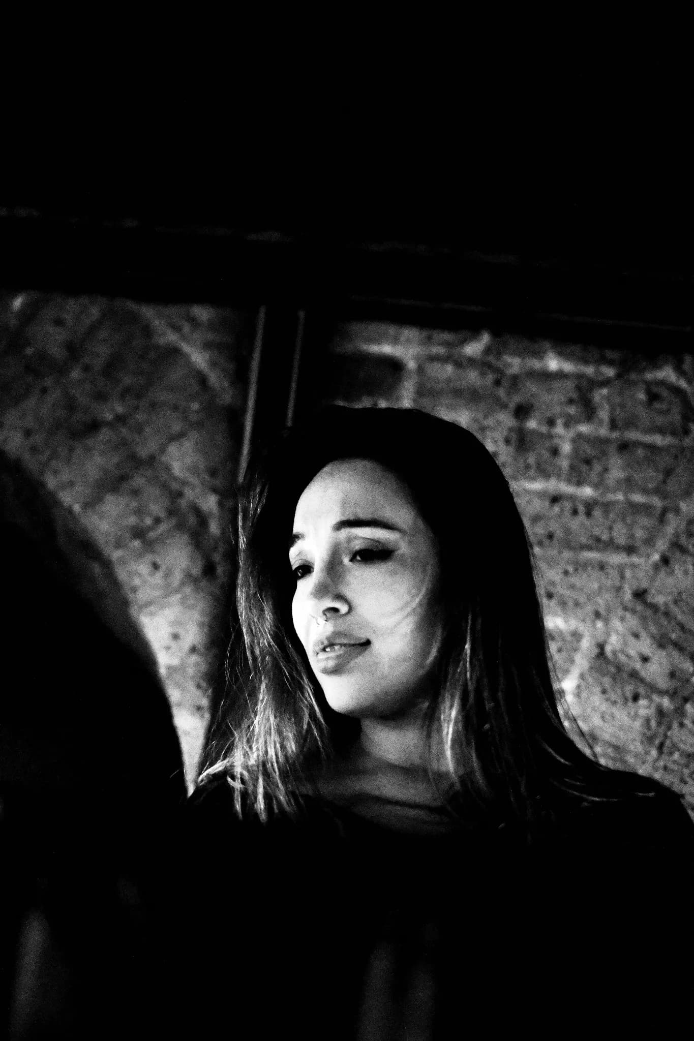 Black and white portrait of a young woman at a milonga against a brick arch