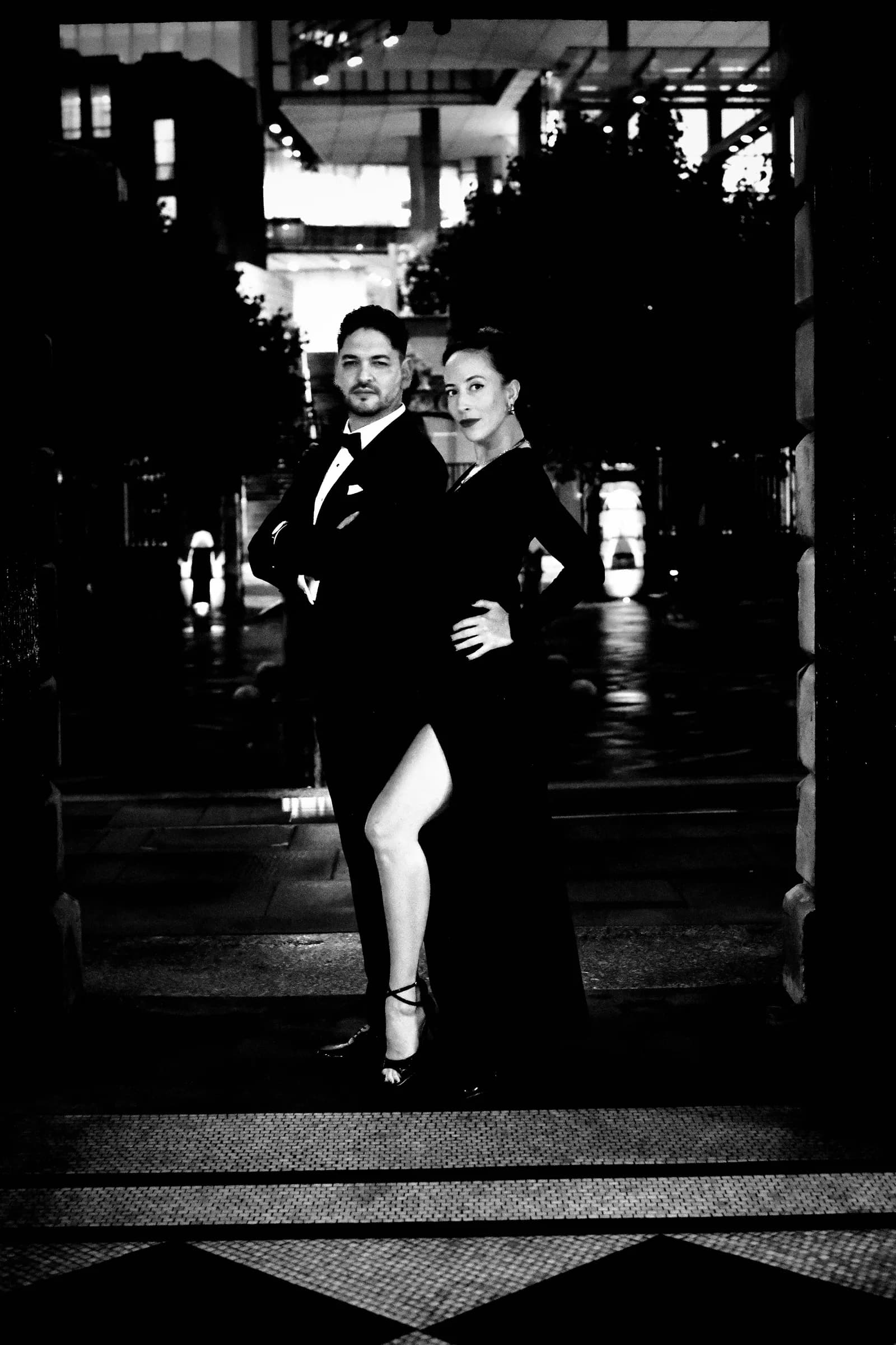 Dancers posed in a dark City of London archway, her leg through the slit of her gown