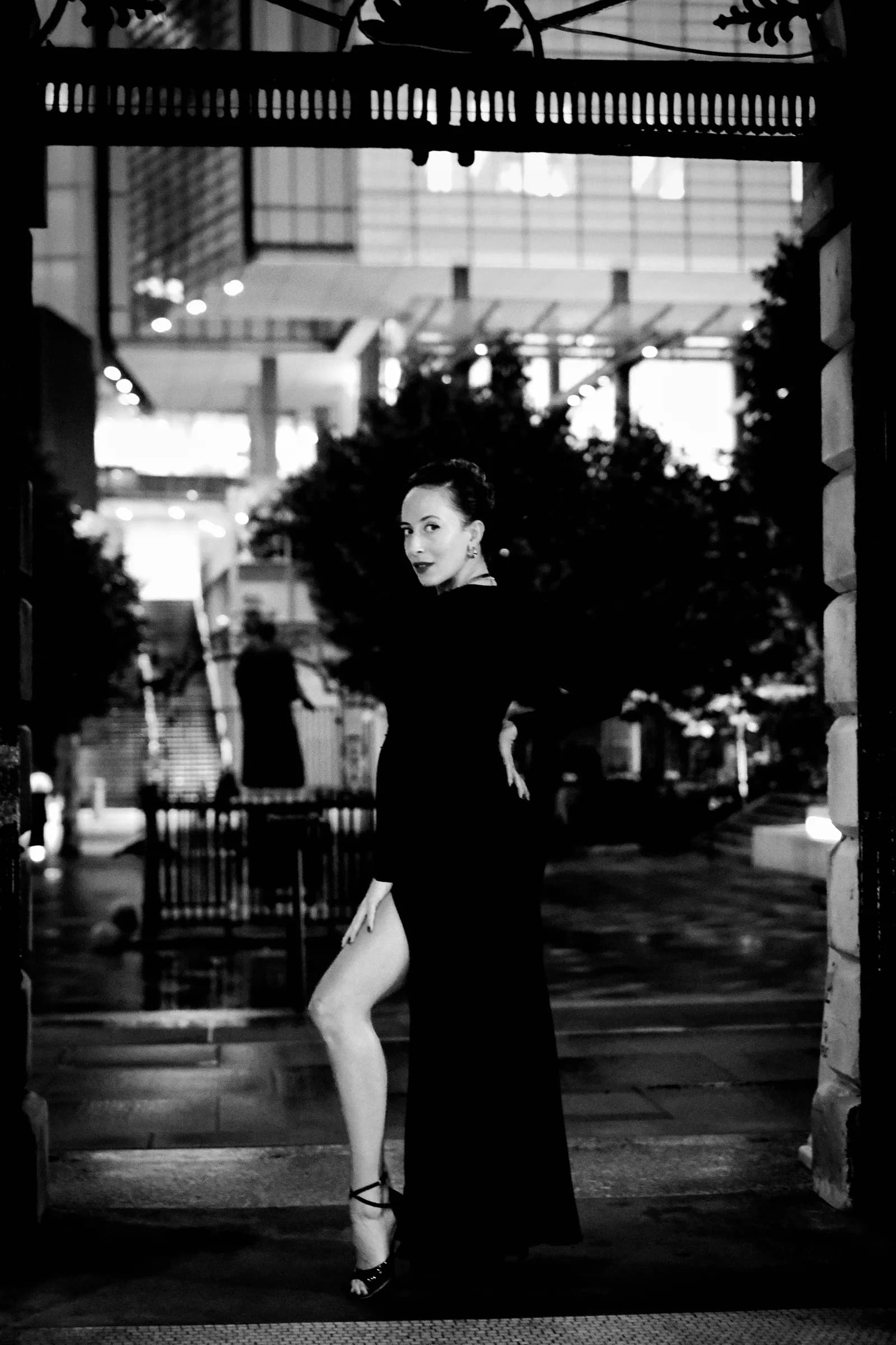 Woman in a black gown glancing back over her shoulder in a lit gateway at night