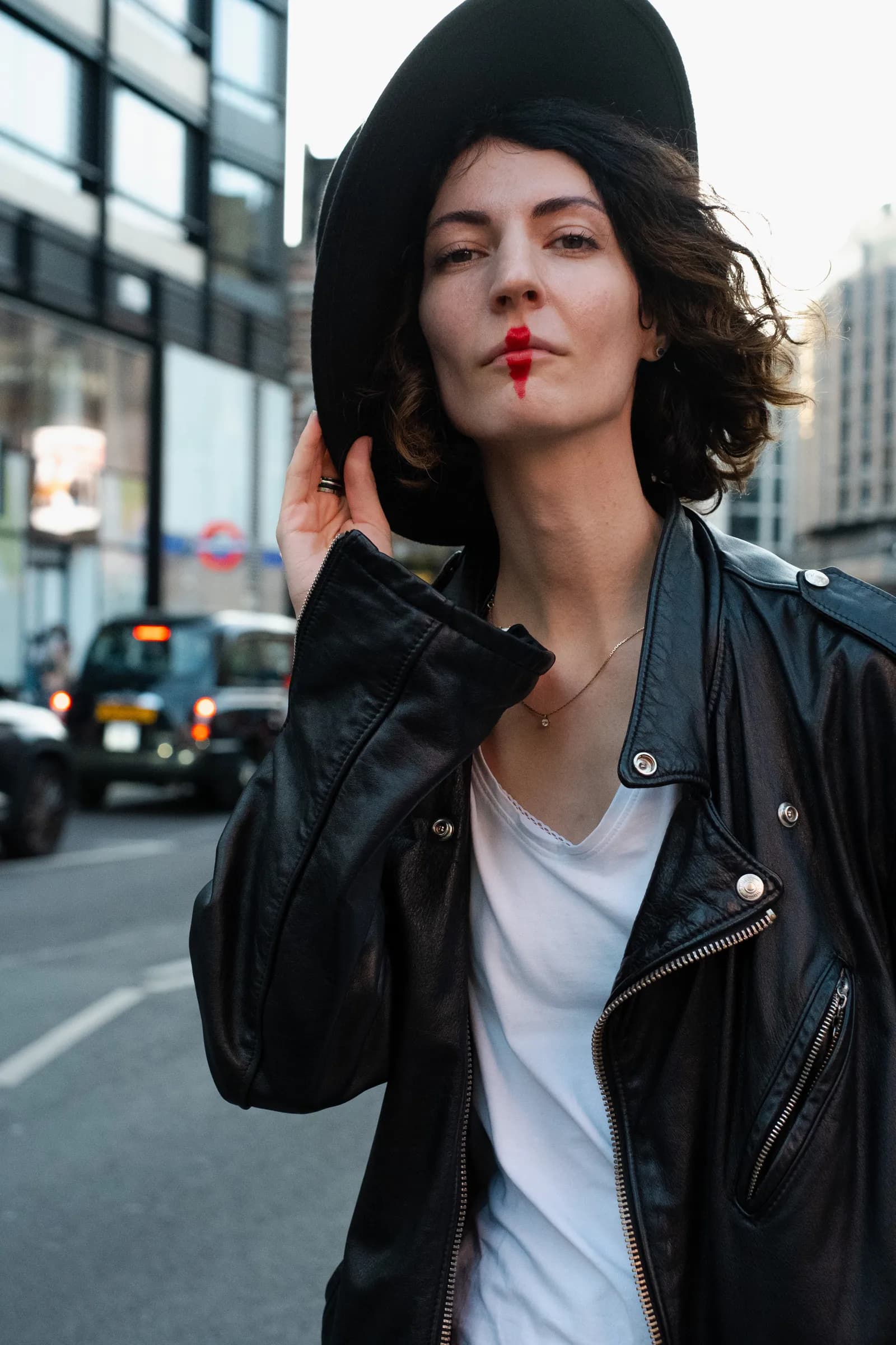 Musician holding her hat brim on a London street, black cab passing behind