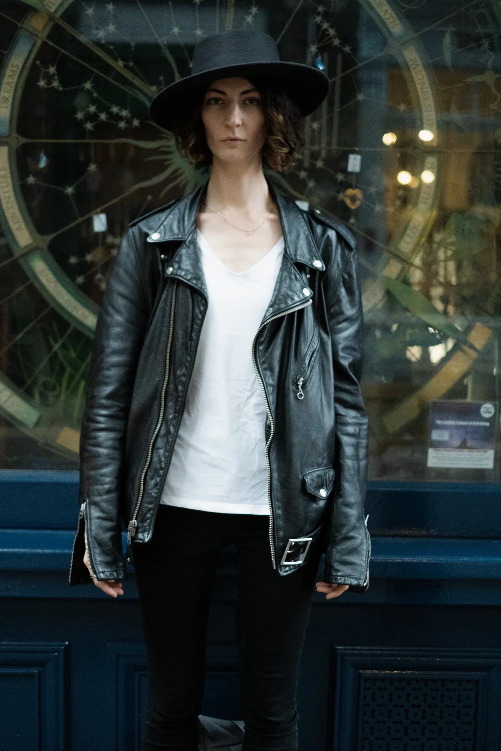 Musician in a leather jacket and hat standing before an astronomical clock shopfront