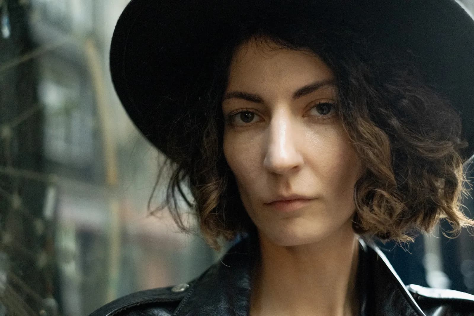 Close portrait under a black hat, jaw set, guitar-street windows behind