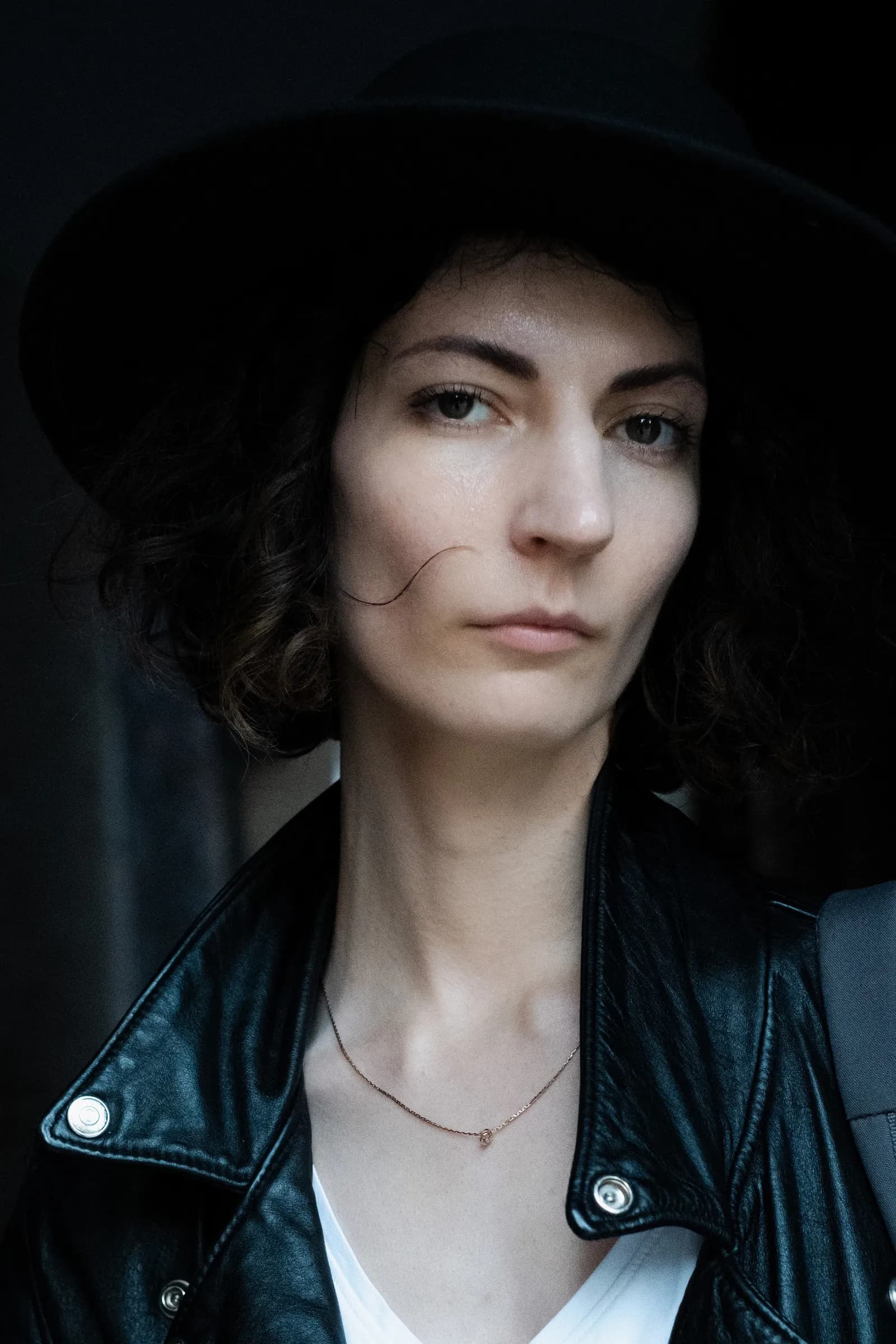 Portrait in a black hat with a stray curl across the cheek, jacket collar up