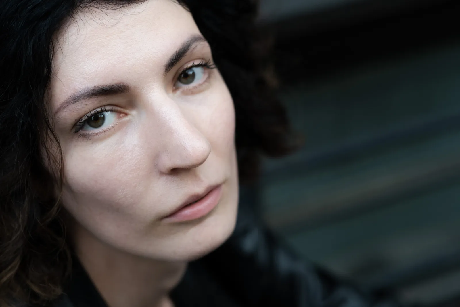 Close portrait of a curly-haired woman, bare-faced, city blur behind her