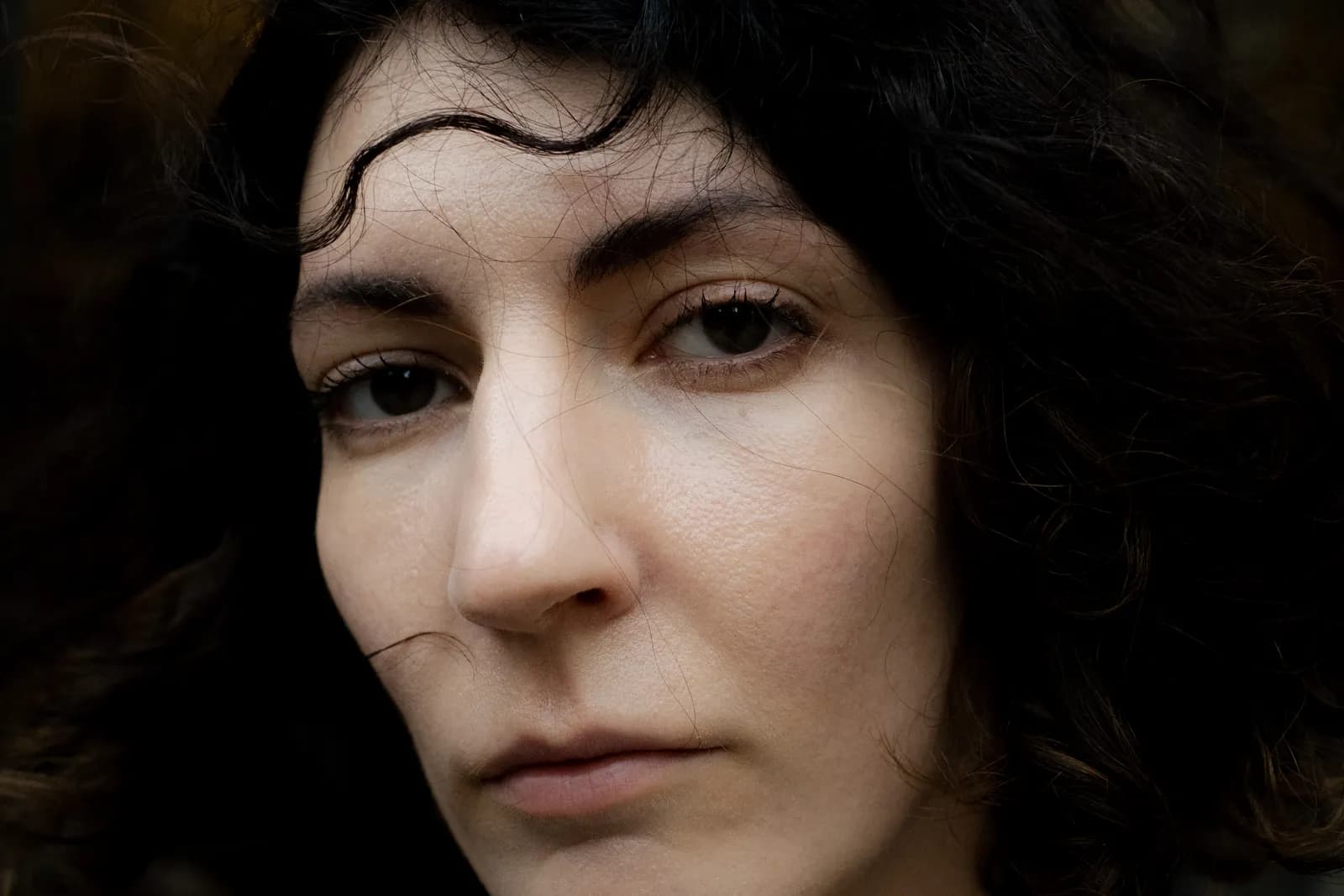 Very close portrait, stray curls across a pale face, dark eyes level
