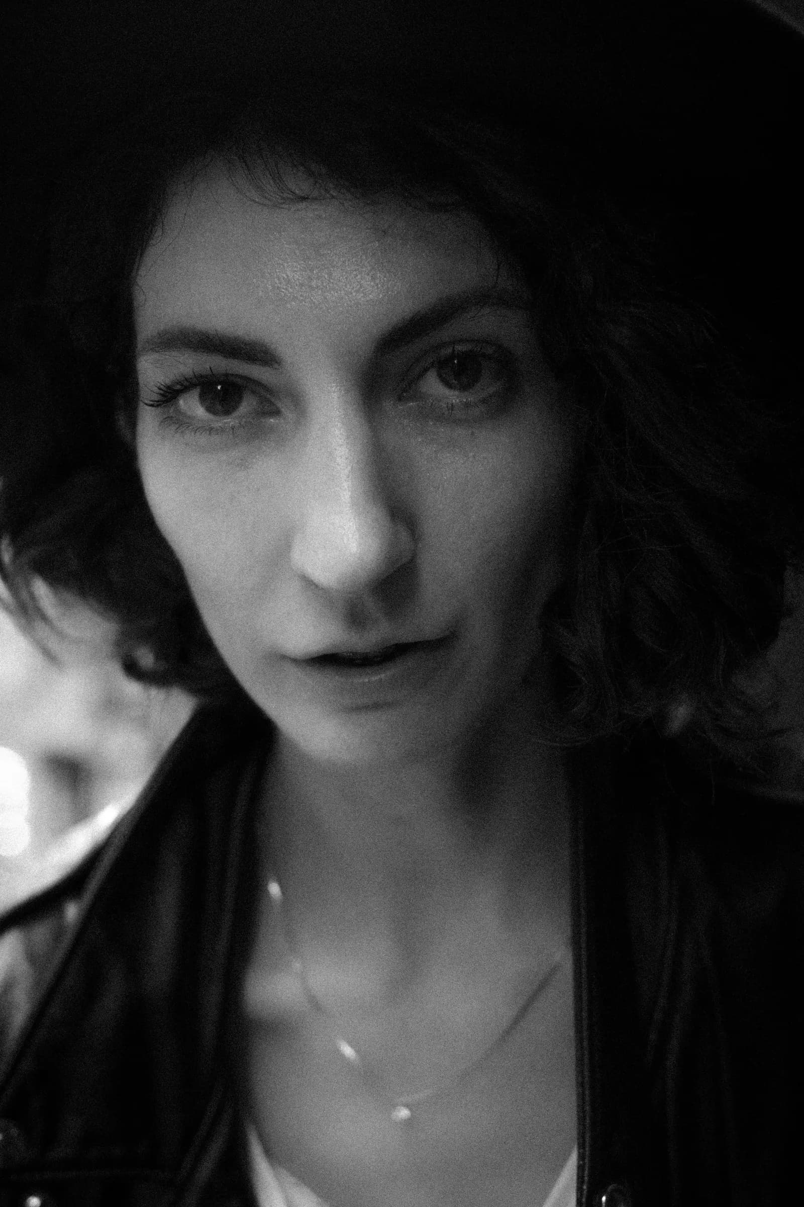 Black and white close portrait under a hat brim, eyes straight into the lens