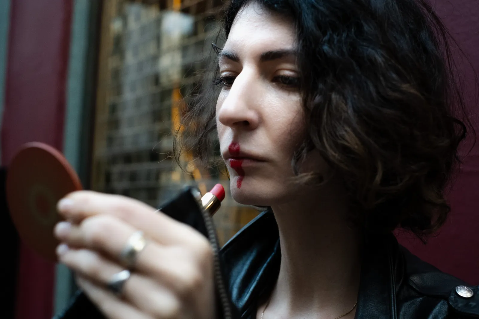 Woman applying red lipstick into a pocket mirror on a lamplit street
