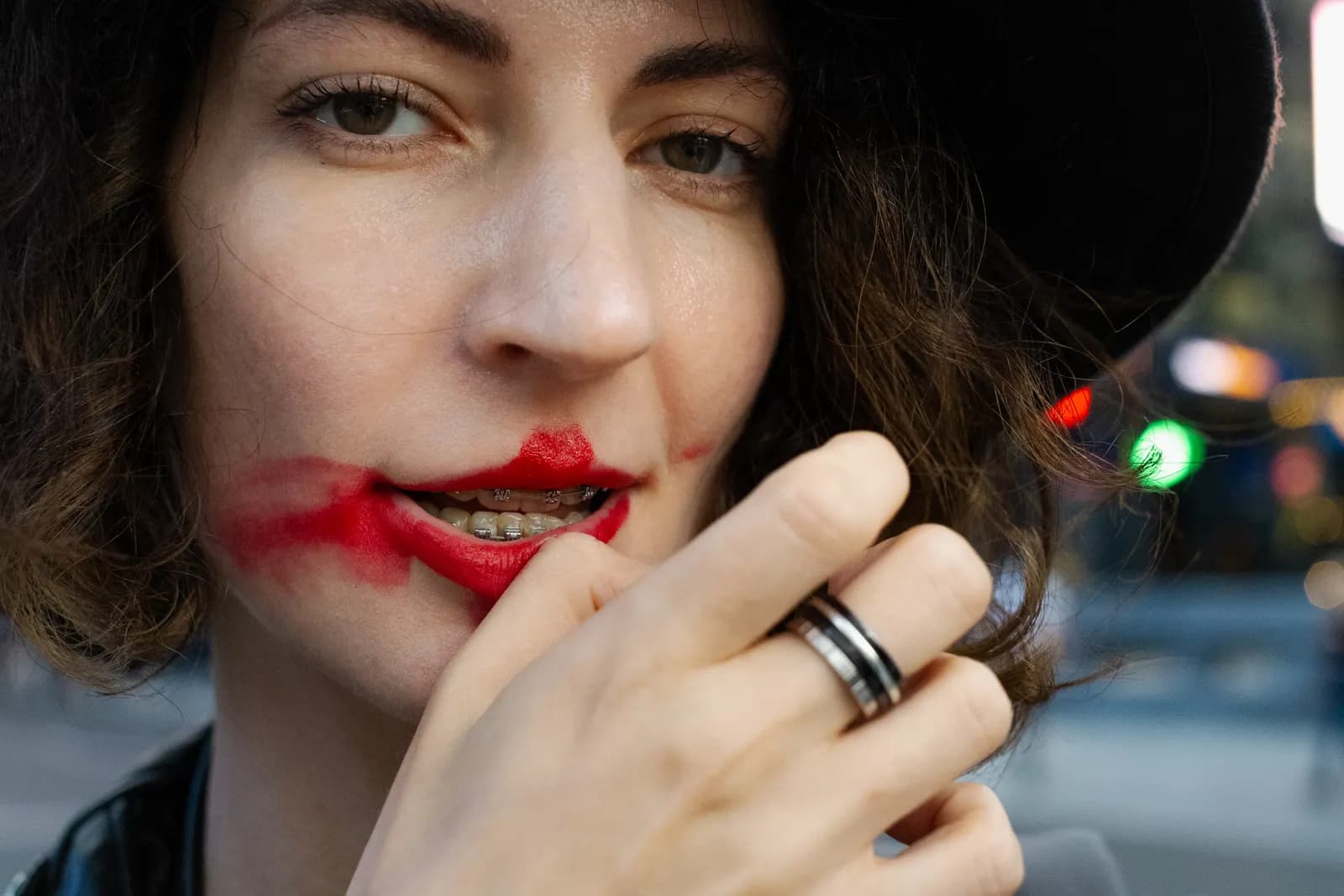 Very close portrait with red lipstick smeared across the cheek, fingers at the mouth
