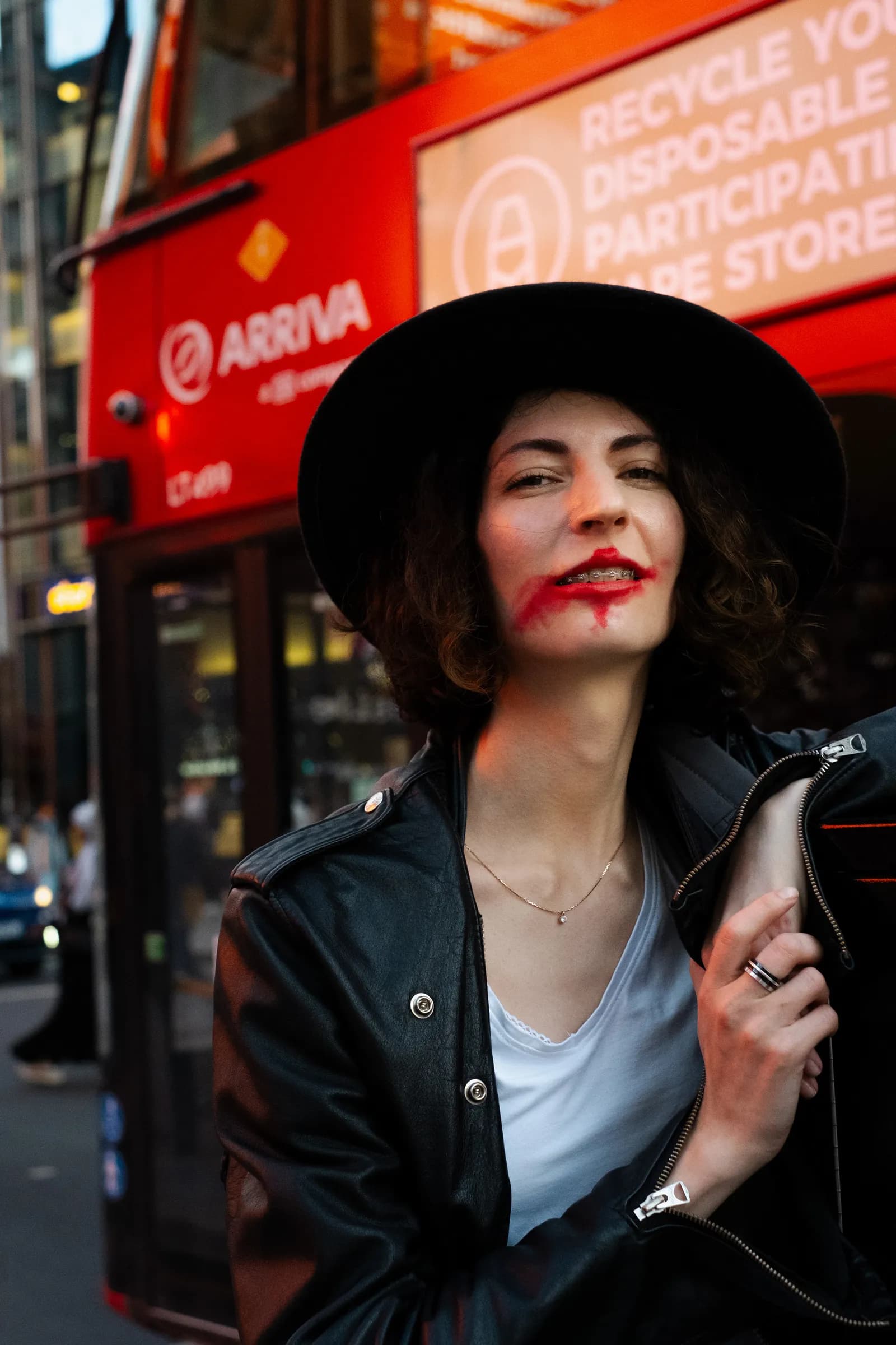 Musician with smeared red lips in front of a red London bus, hat tilted