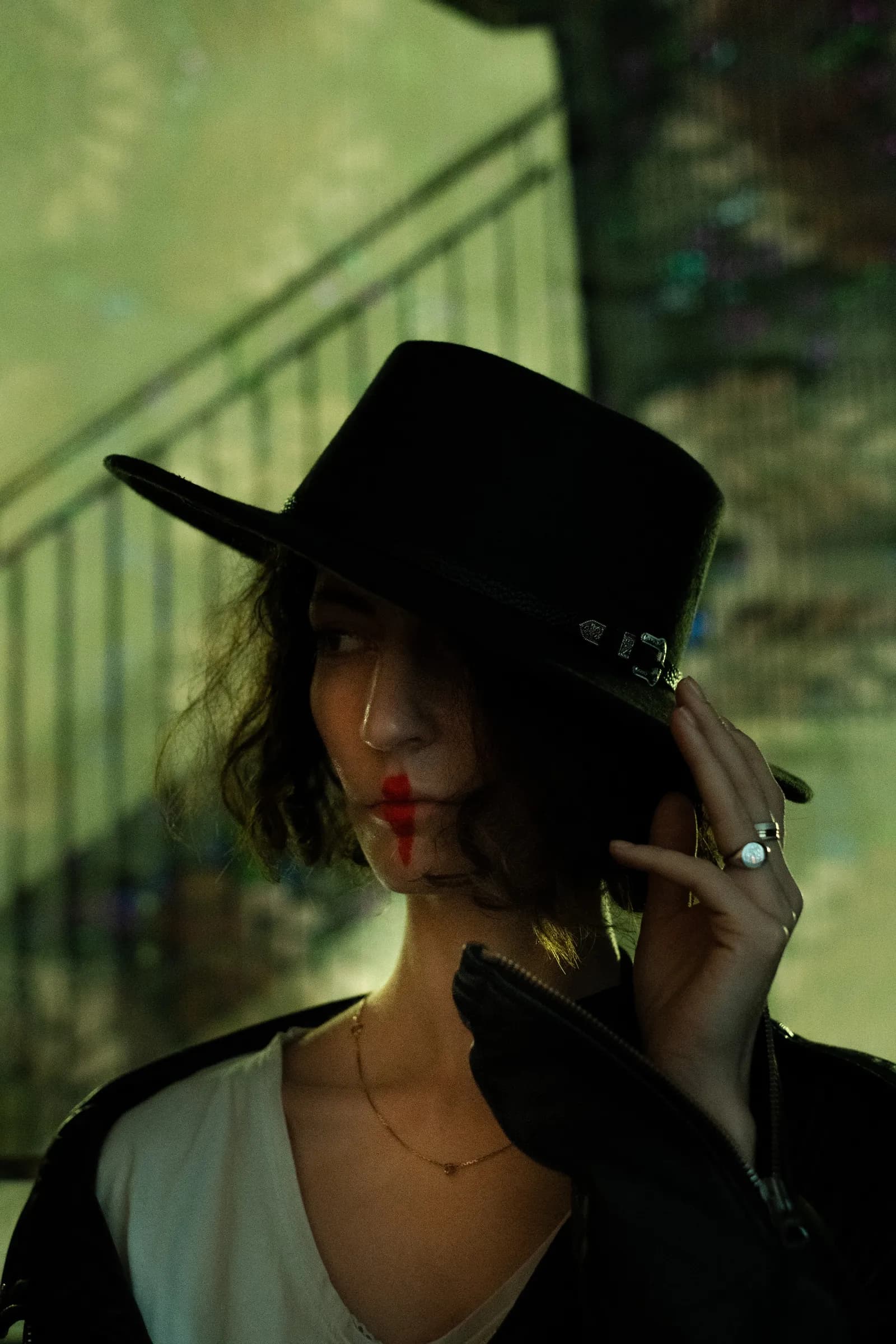 Face half-hidden under a hat brim in green streetlight, red lips catching the glow