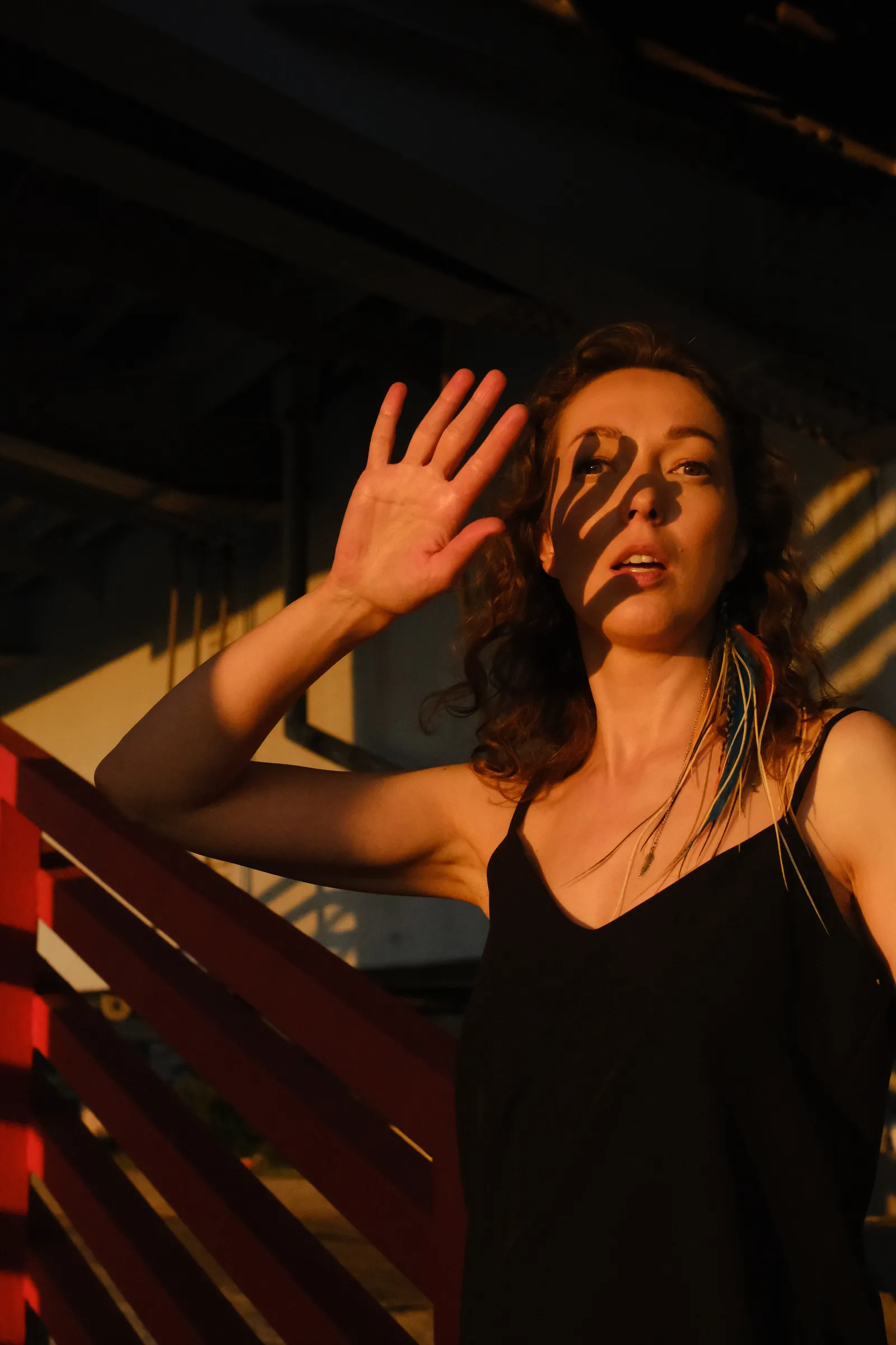Woman raising a hand against the low sun, cable shadows striping her face