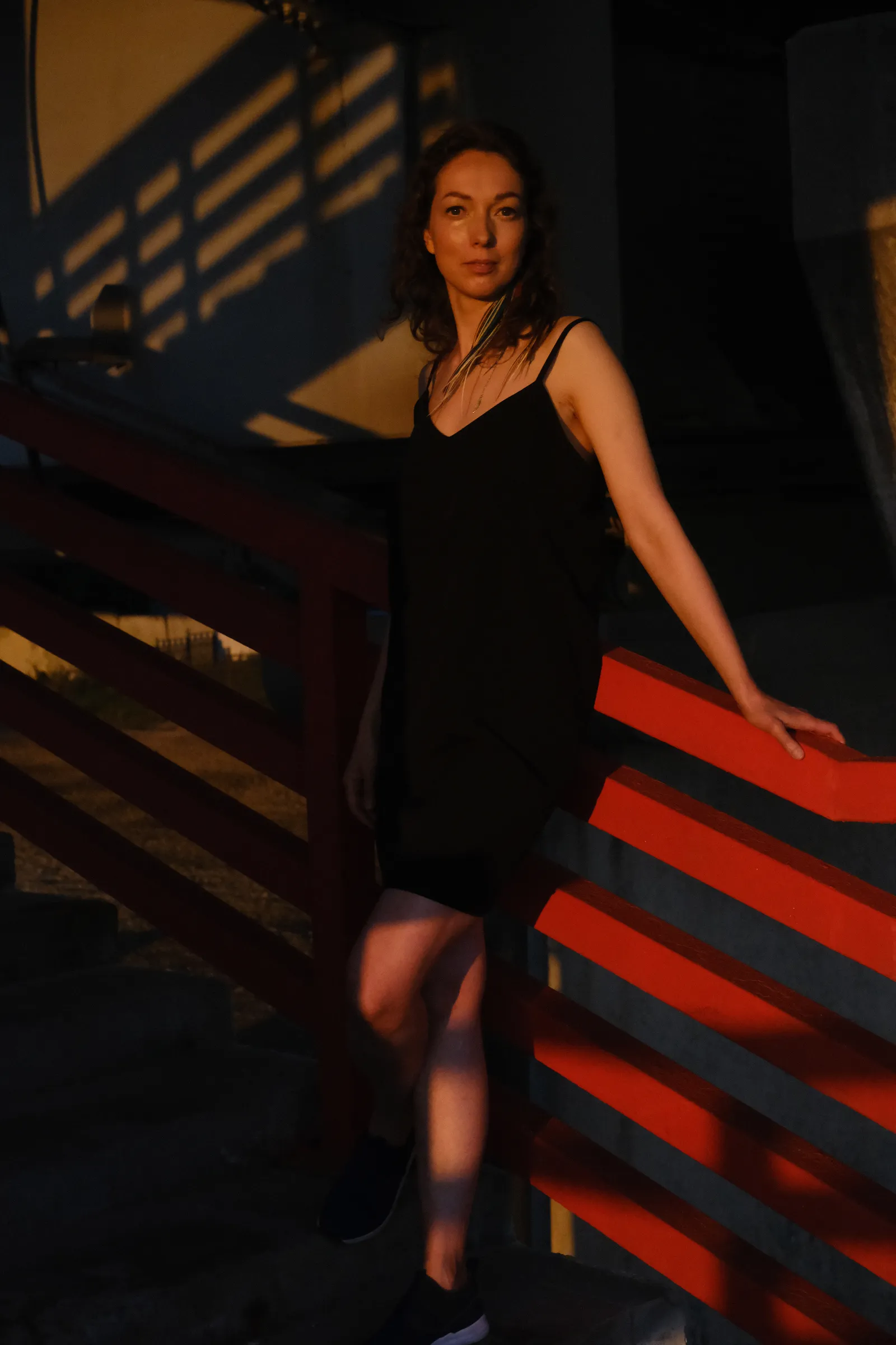 Woman on red-railed steps in hard evening light, shadows laddered up the wall