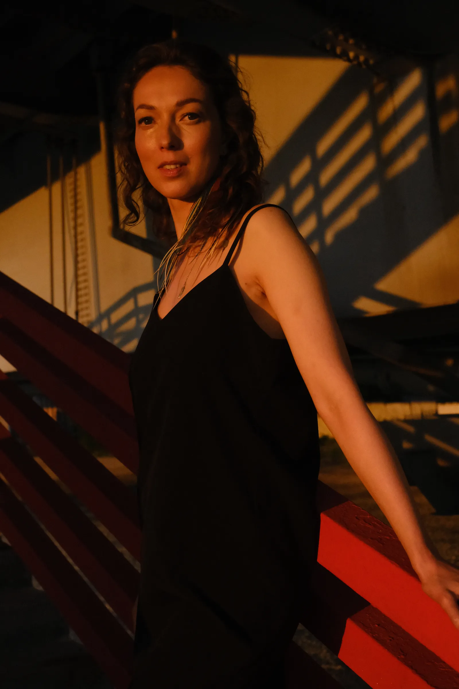 Woman in a black slip dress on a stairway in golden light, wet strands at her face
