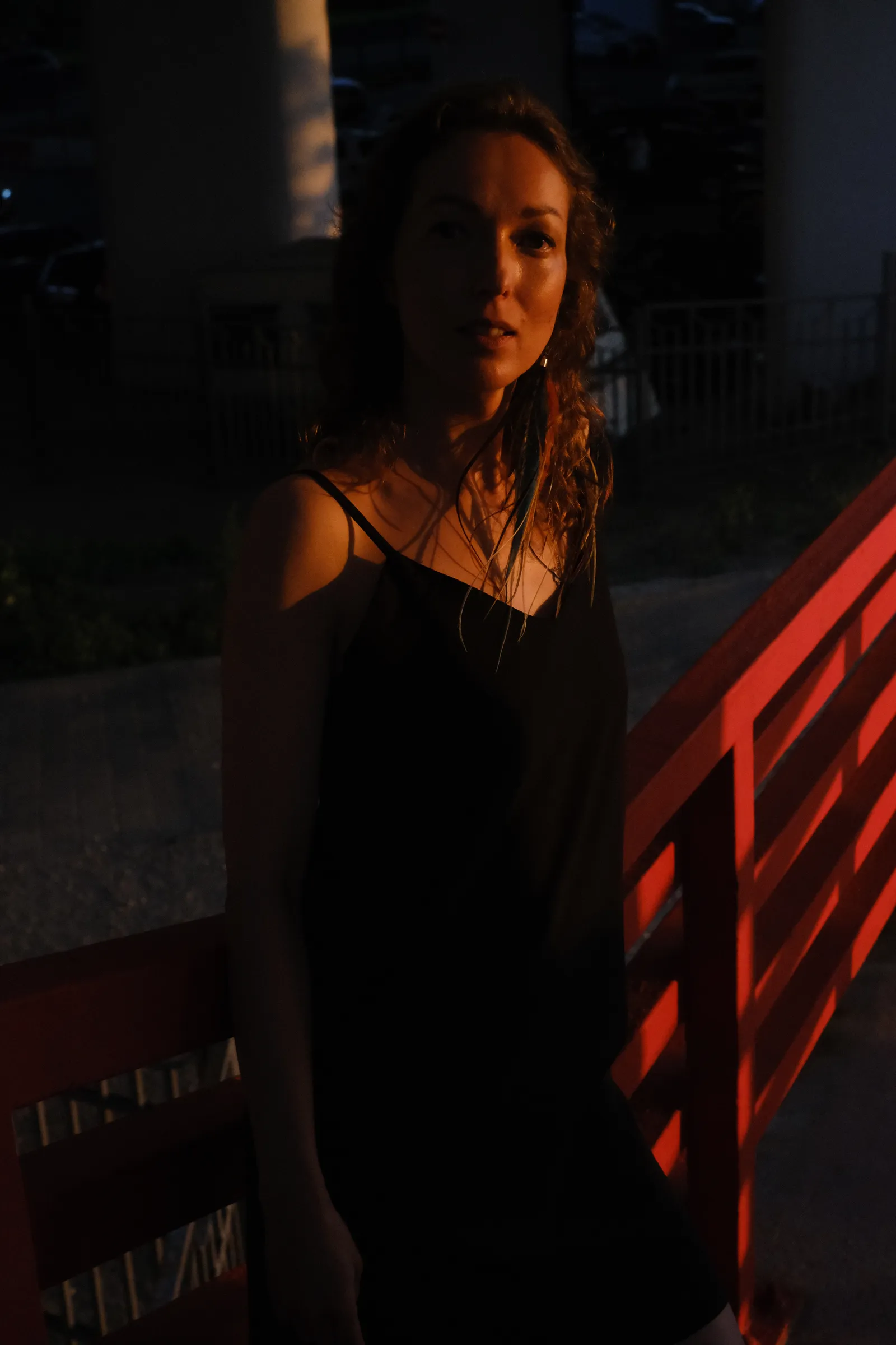 Woman in a black dress at a red rail in the last direct sun, half of her already in shadow