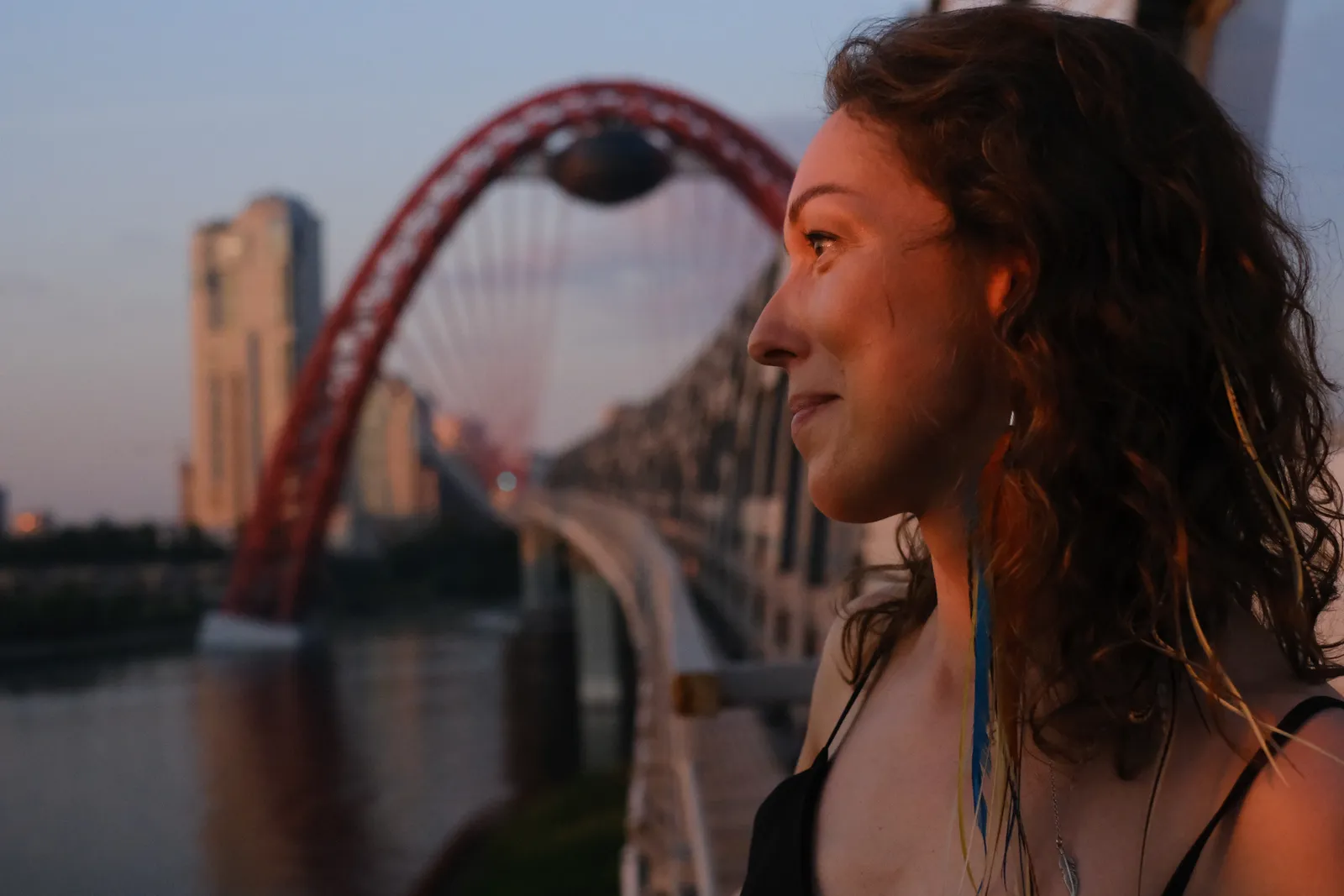 Profile of a smiling woman on the bridge walkway, red arch and towers behind