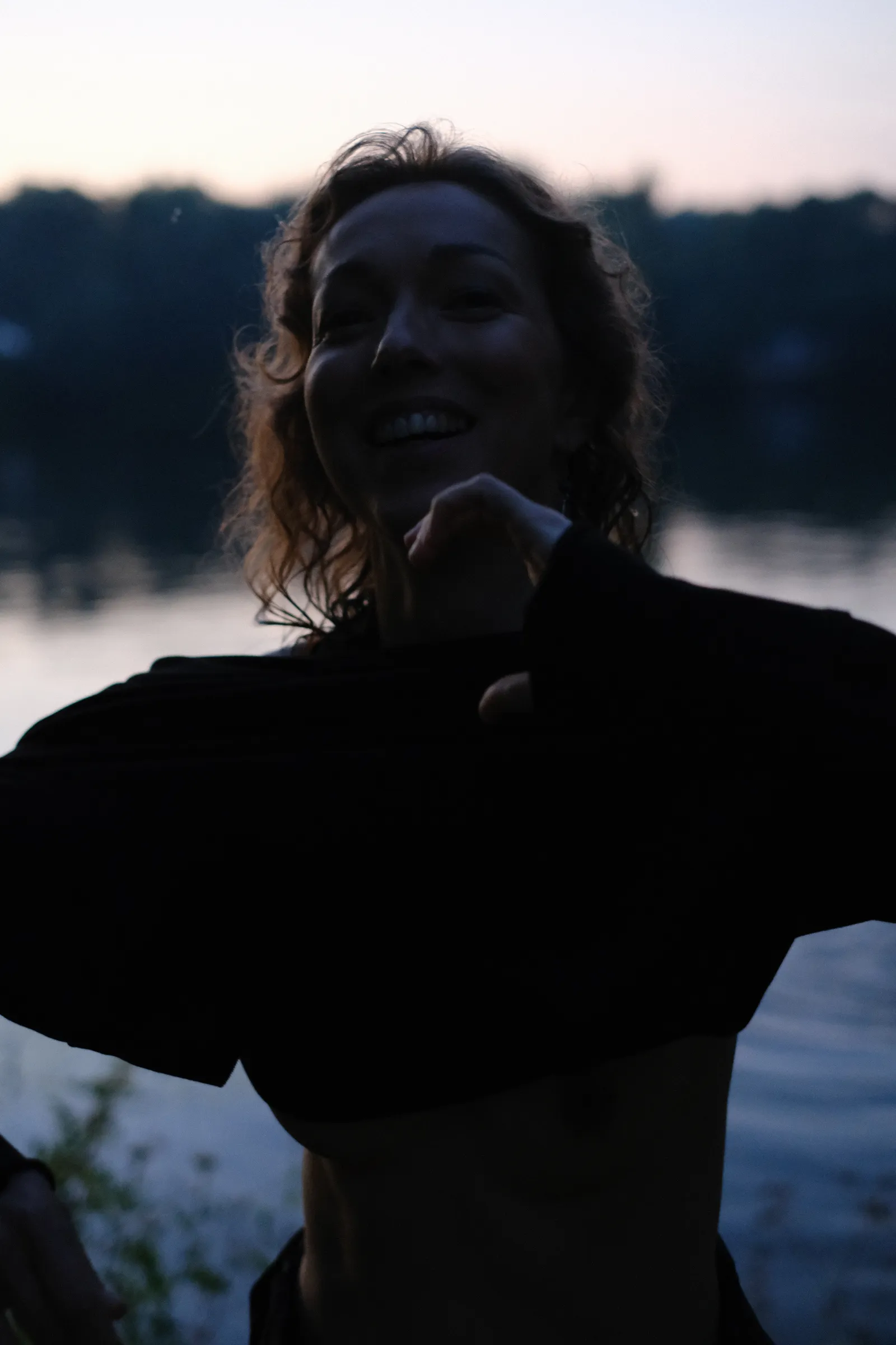 Laughing woman pulling her black dress over her head against the pale river
