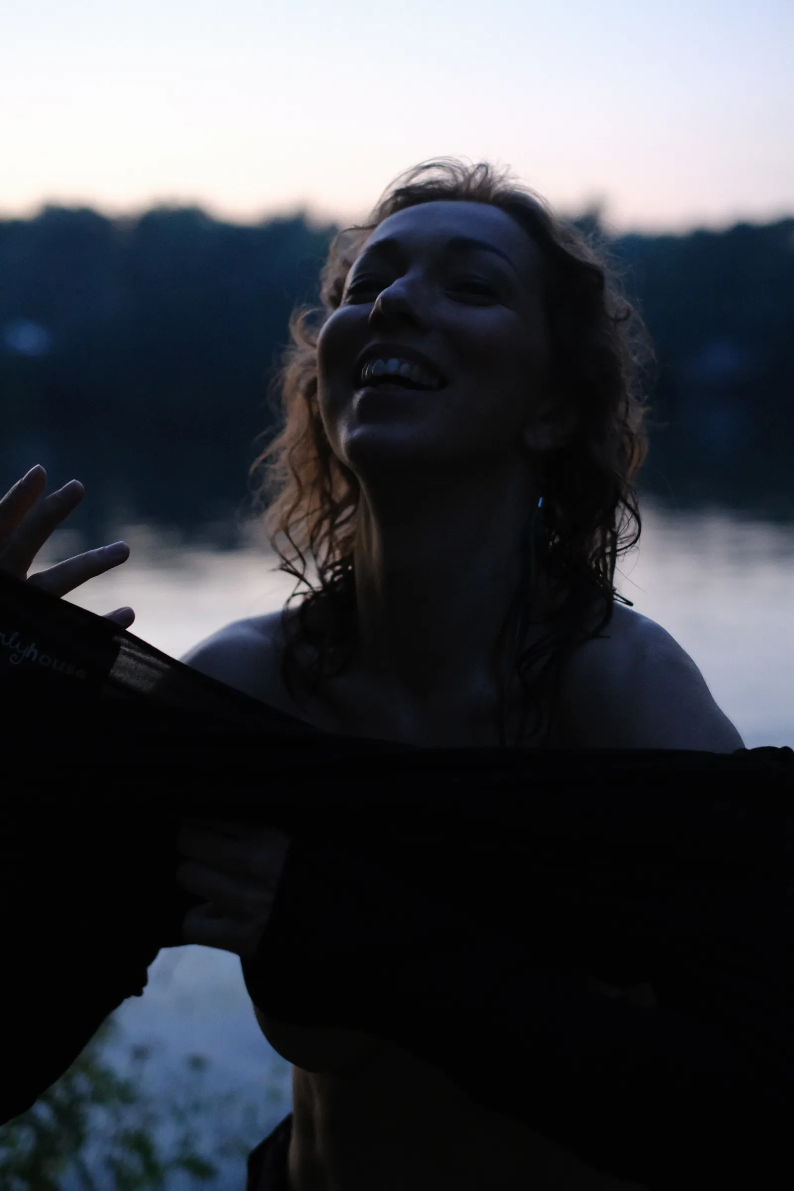 Woman laughing with her head thrown back as she pulls off the dress at dusk