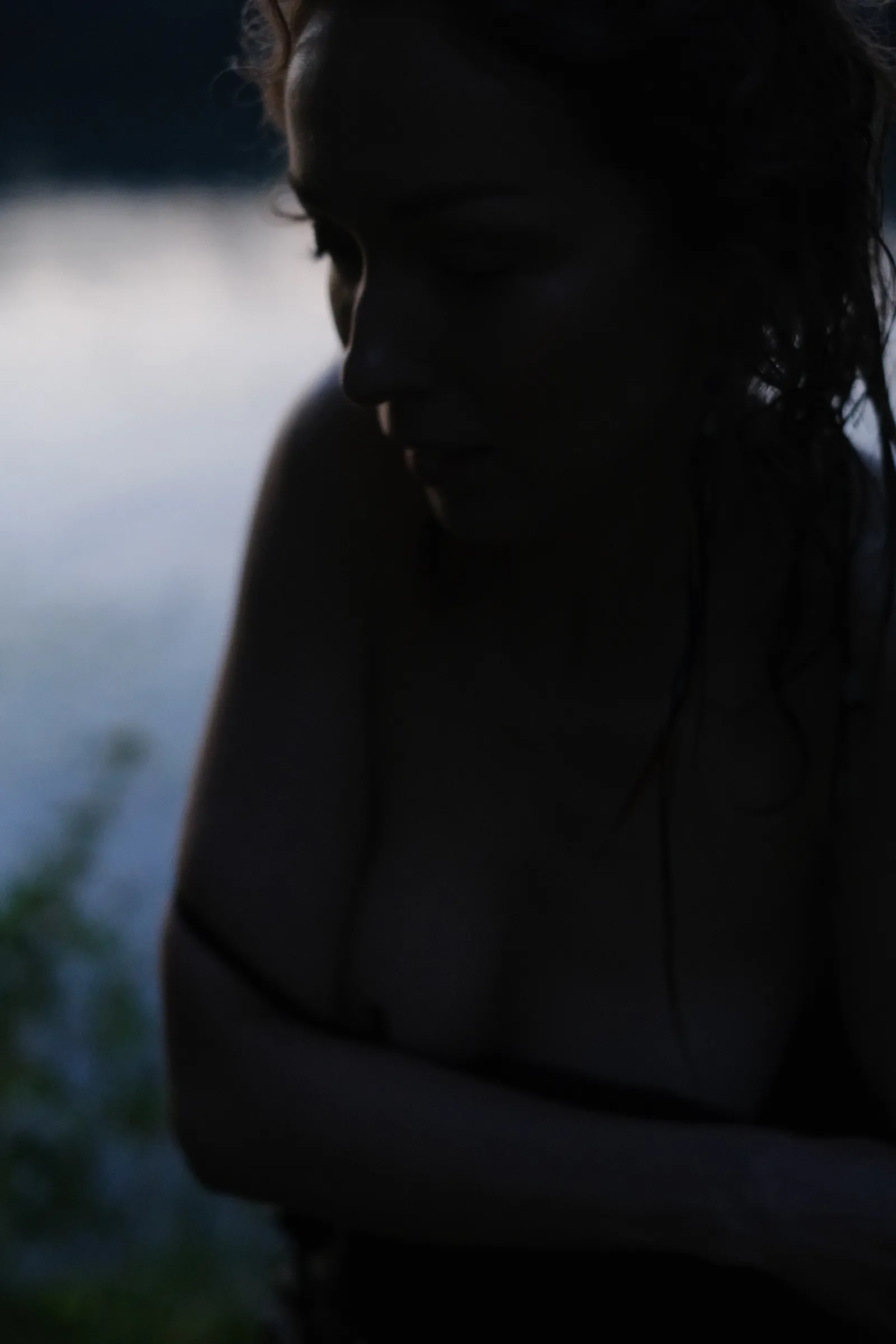 Silhouetted woman at the river in failing light, strap fallen from her shoulder