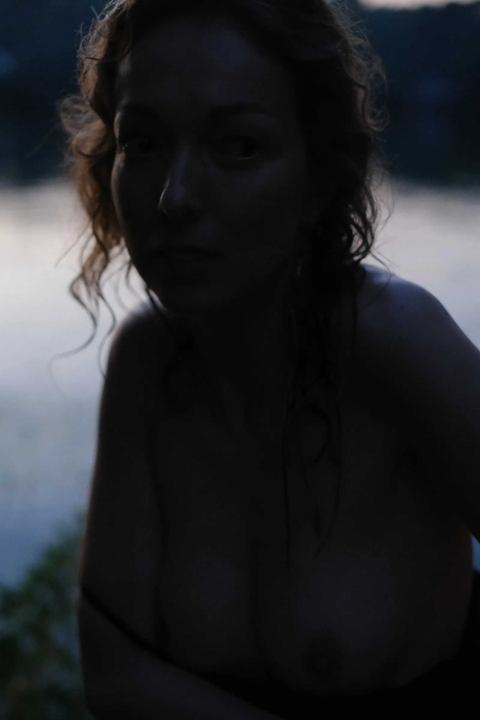 Woman leaning towards the lens in the last light, wet curls, bare shoulders