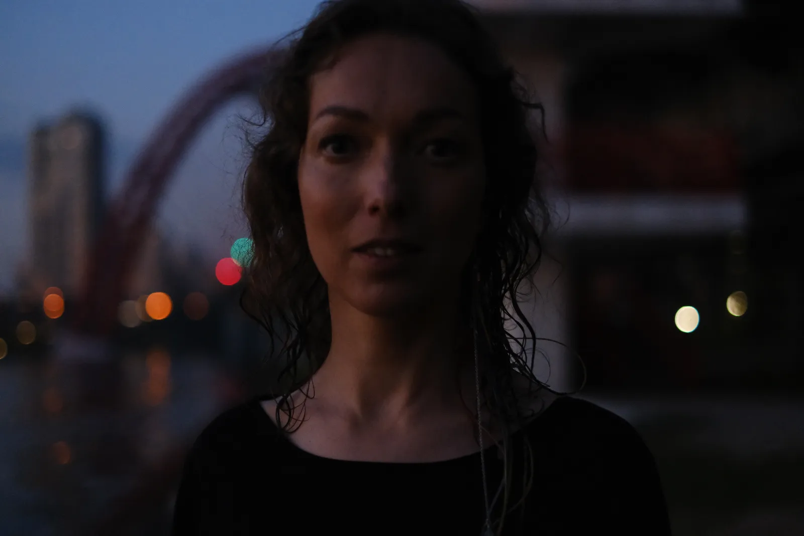 Close dusk portrait, city lights dissolved into coloured points behind her