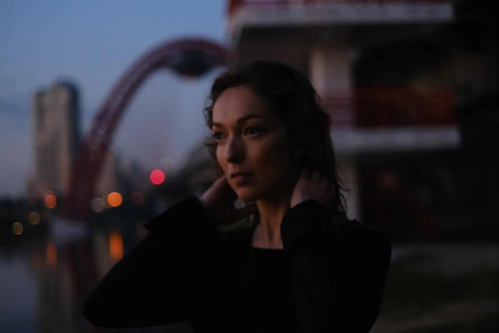 Woman with wet hair at the embankment at blue hour, the red bridge lit behind her