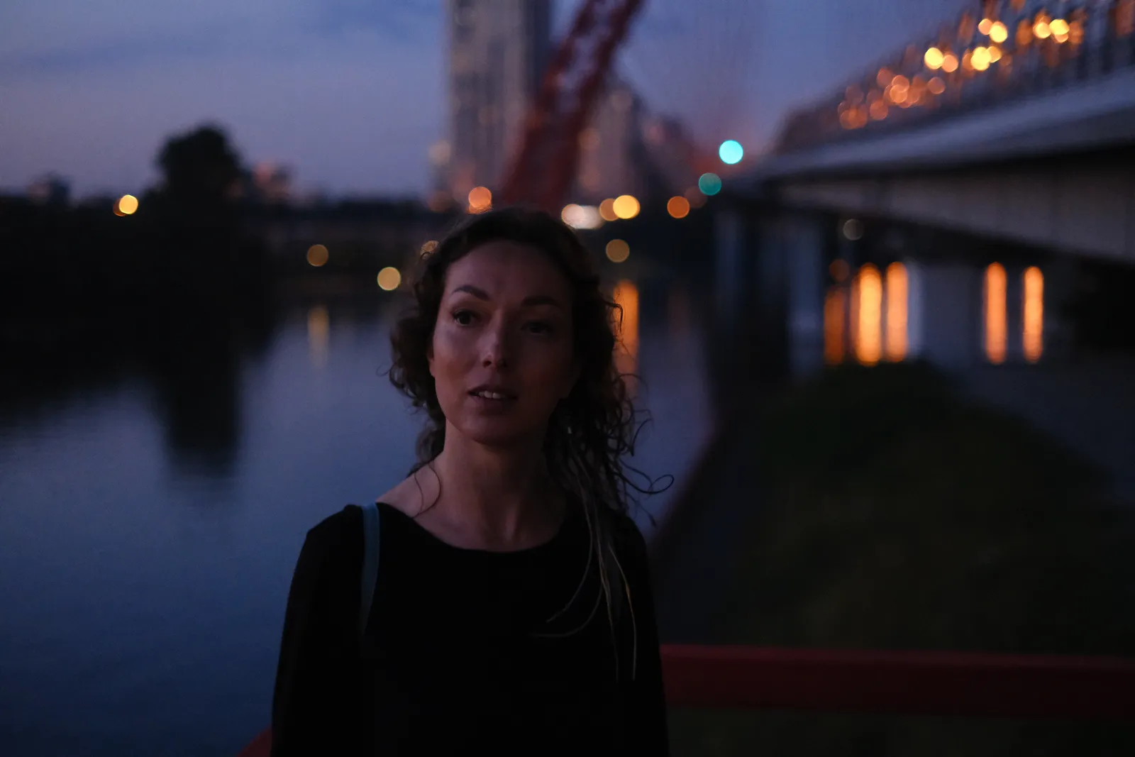 Woman with wet curls under the lit span of the bridge at night