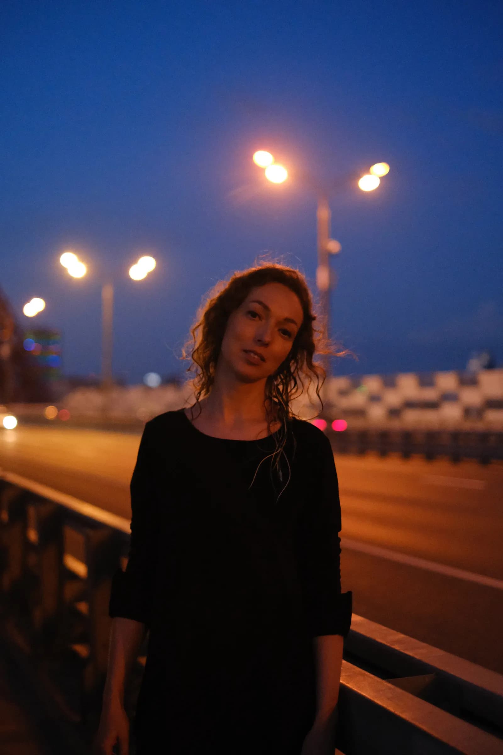 Woman in black on the night bridge under a run of streetlamps