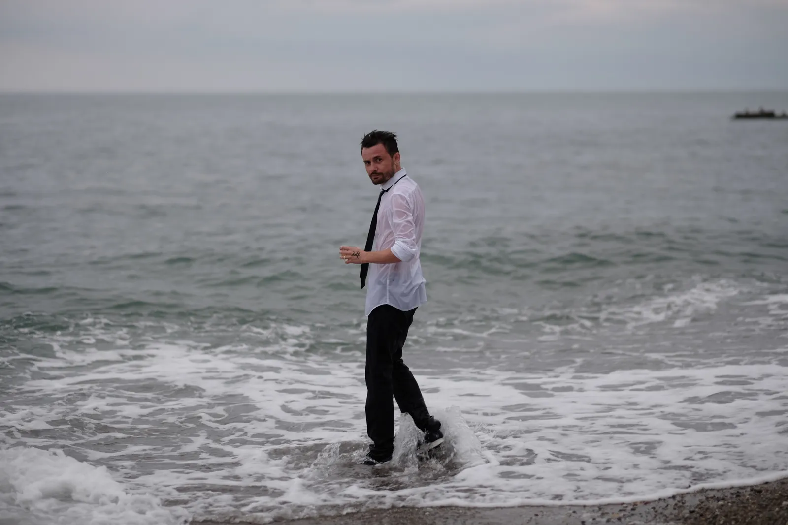 Man wading out of the surf in a soaked white shirt, glancing back