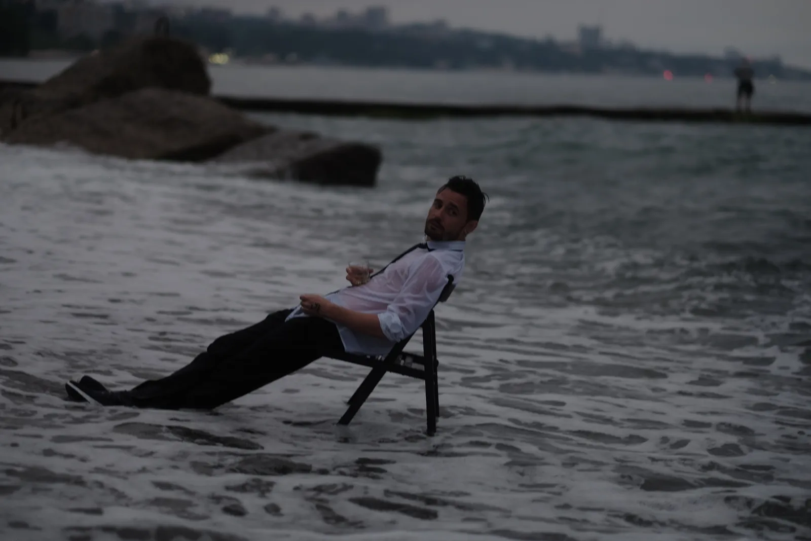 Man in a white shirt tipping back on a chair planted in the surf at dusk
