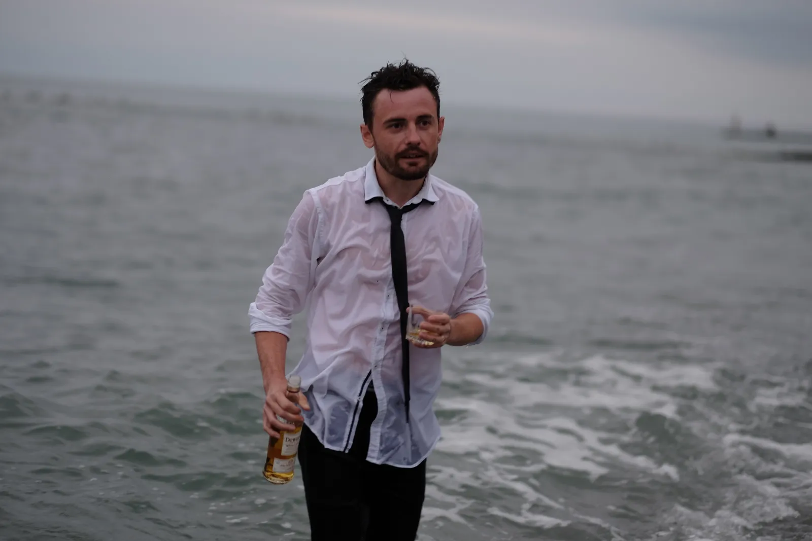 Man standing waist-deep in the sea with a bottle, shirt soaked through