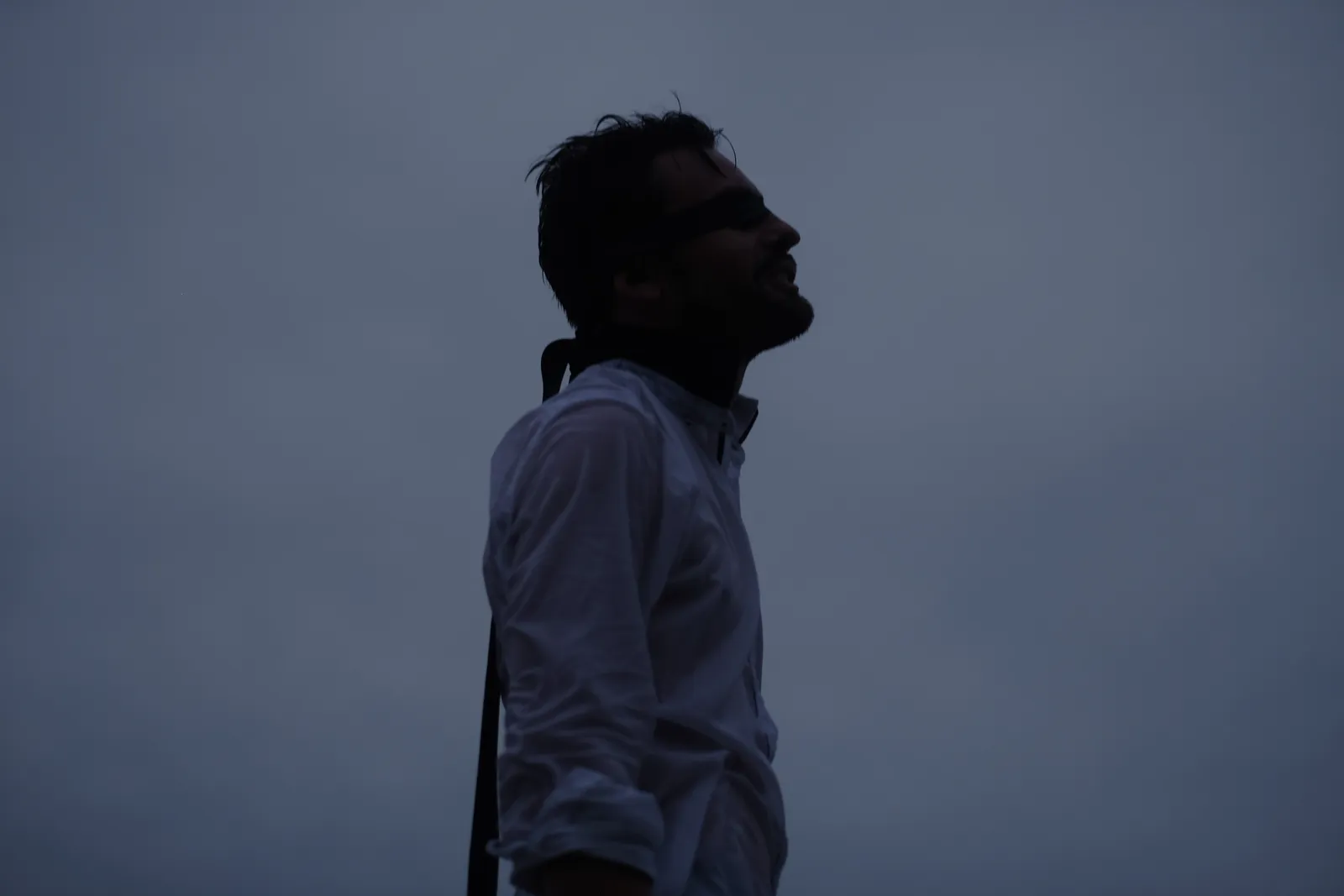 Silhouette of a man in a white shirt against a grey-blue evening sky, face lifted