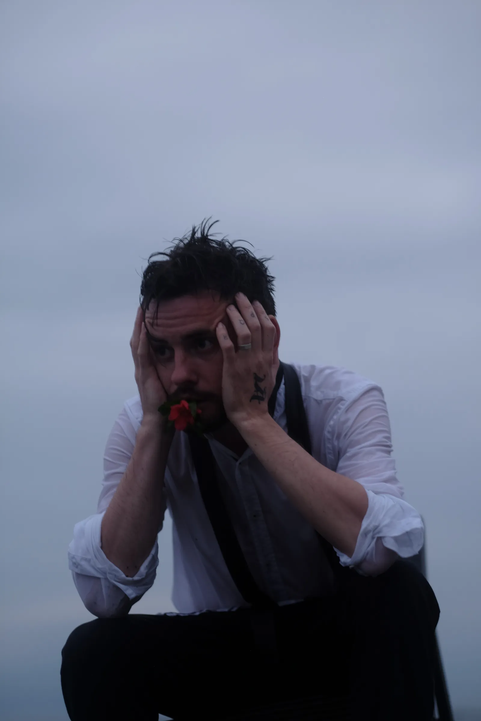 Man crouched on the shingle with his head in his hands, wet hair on end