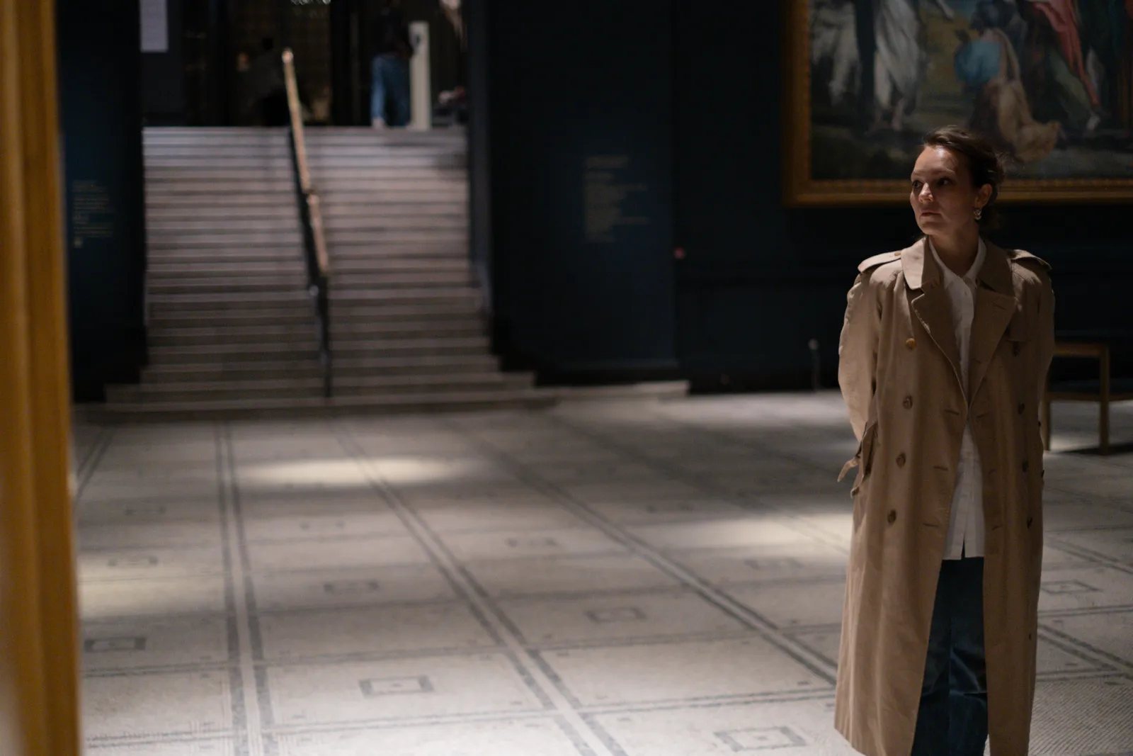 Woman standing in an empty museum hall, staircase rising behind her