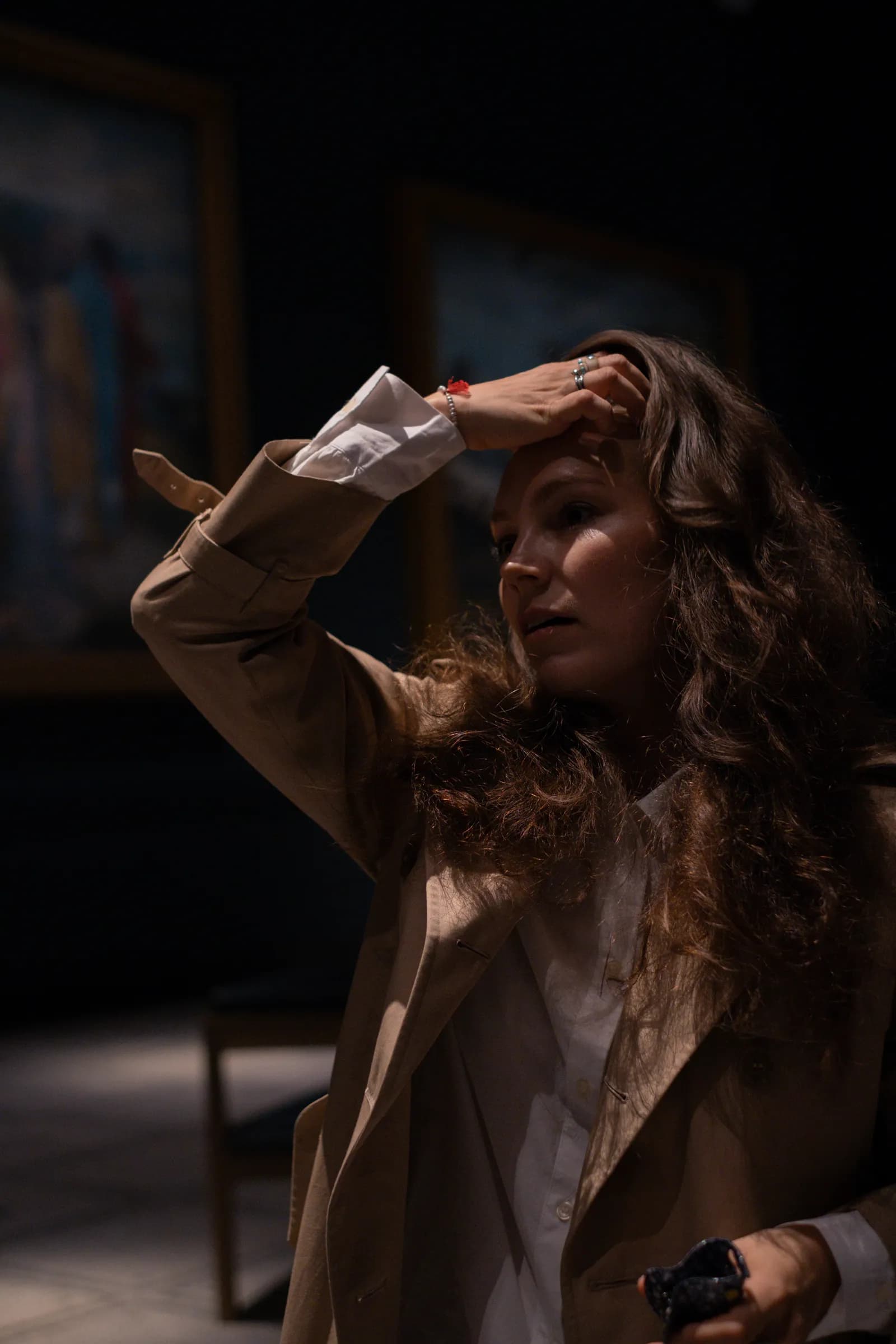 Long-haired woman shielding her eyes with her hand in a dark picture gallery