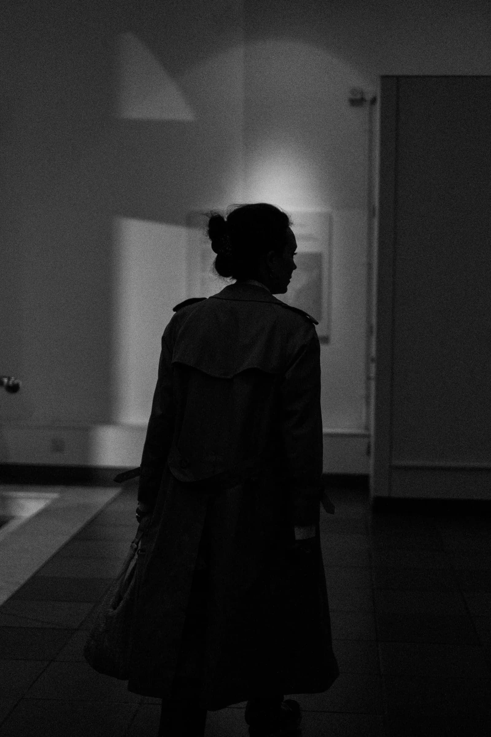 Dark silhouette of a woman in a trench walking away through a museum gallery