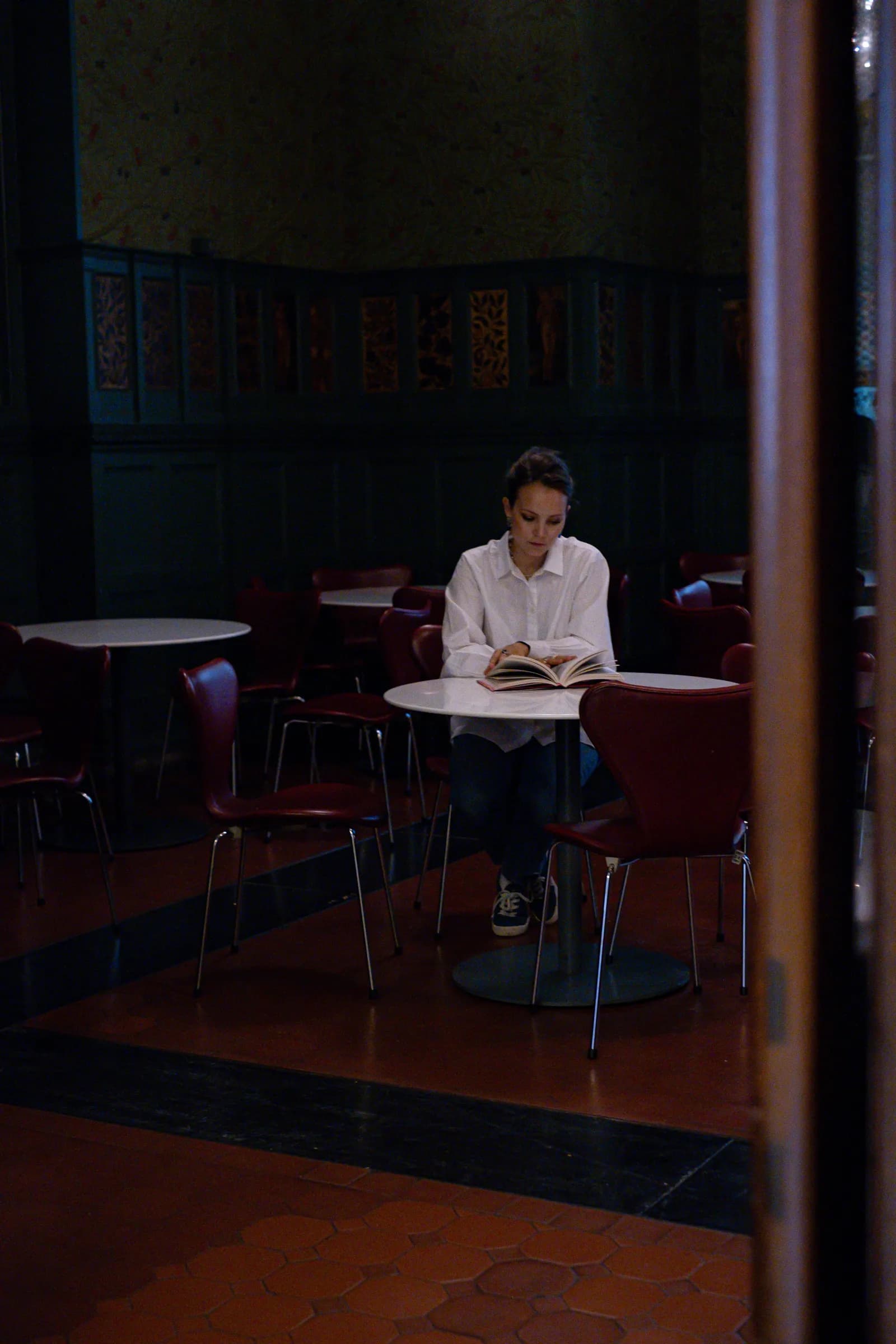 Woman alone with a book at a small round table in an empty museum cafe