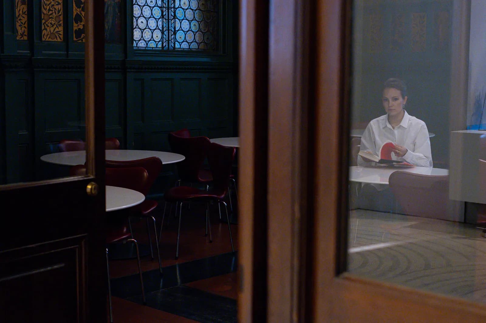 Reader at her table seen through the glass of a green panelled door