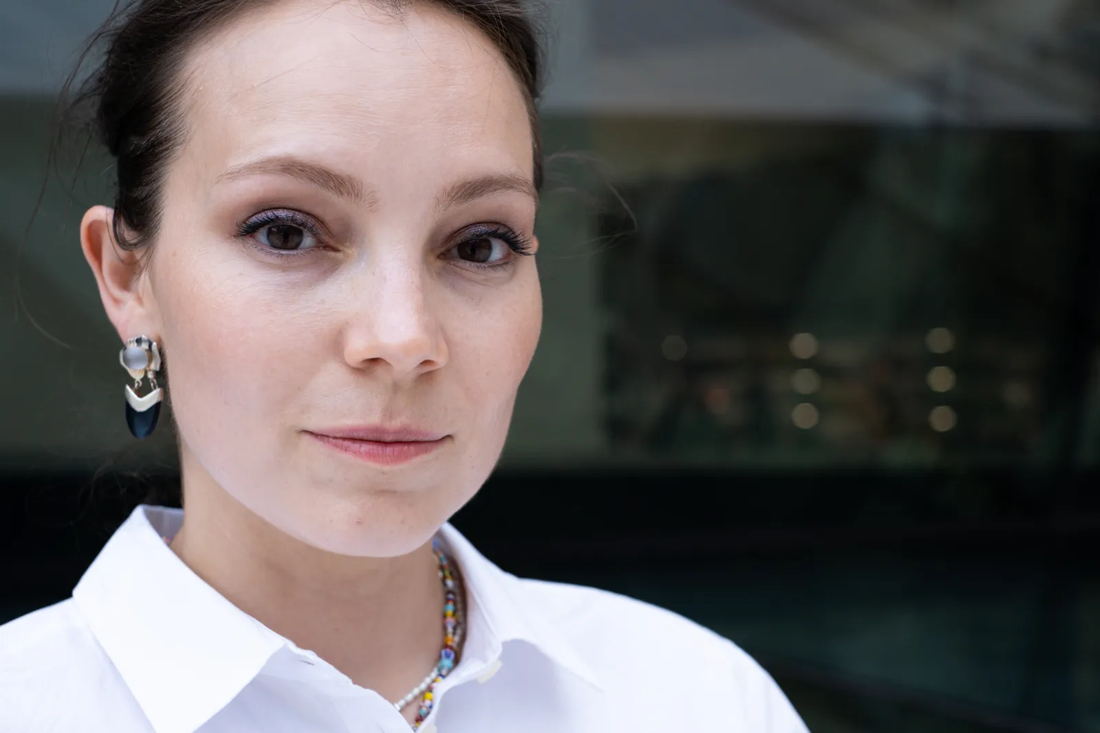 Close portrait of a woman in a white shirt with drop earrings, looking into the lens