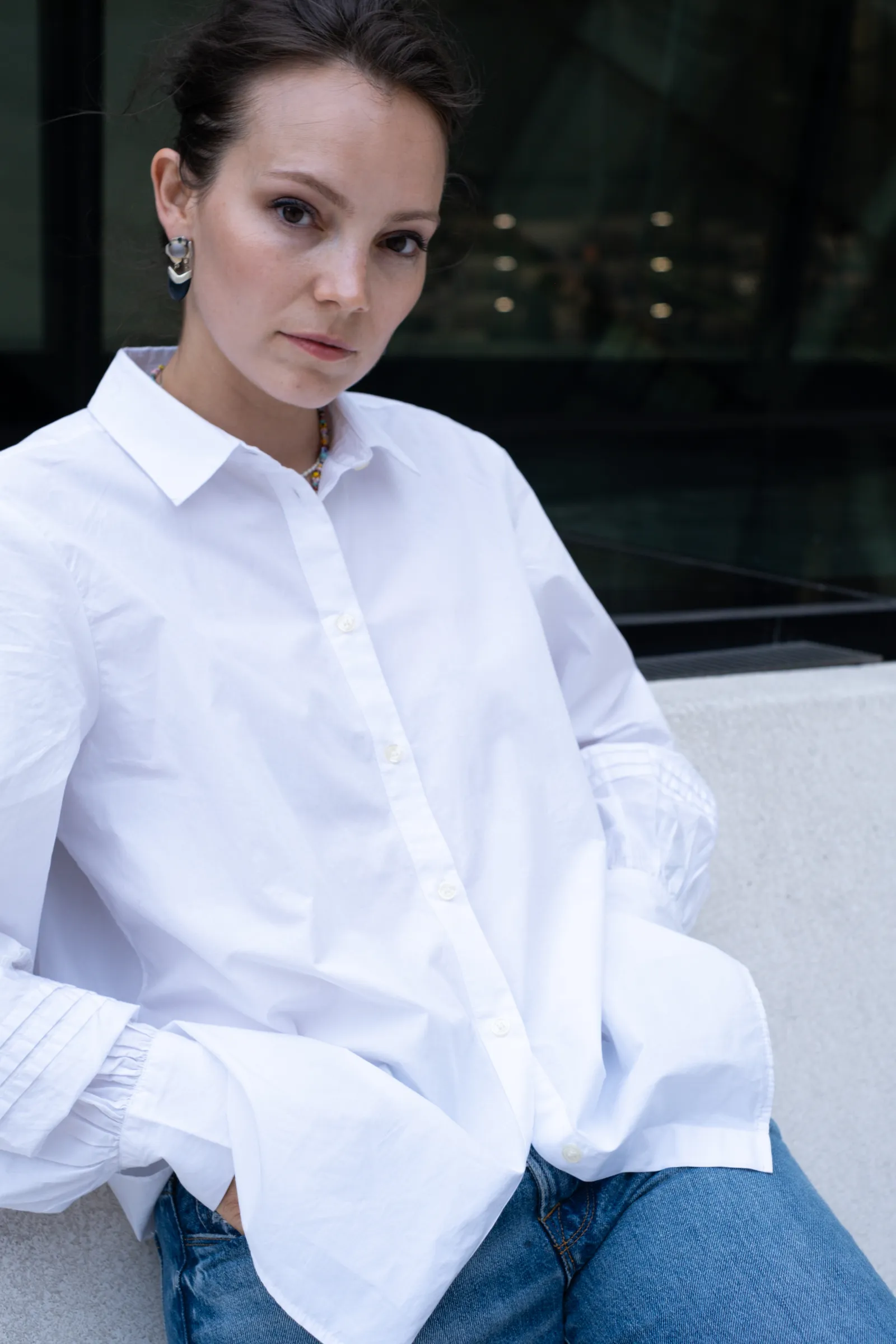 Close portrait in a crisp white shirt with drop earrings, gaze steady