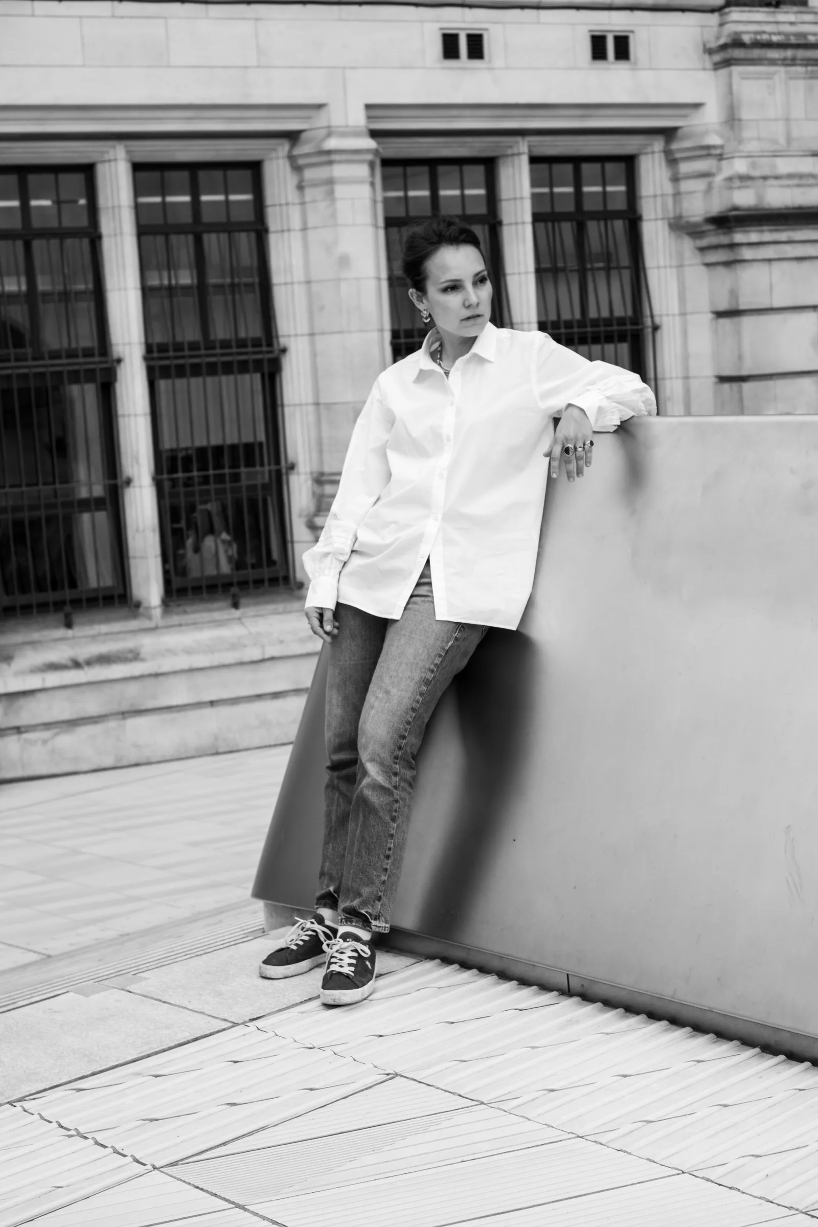 Black and white figure in a white shirt leaning against a stone parapet in a museum courtyard