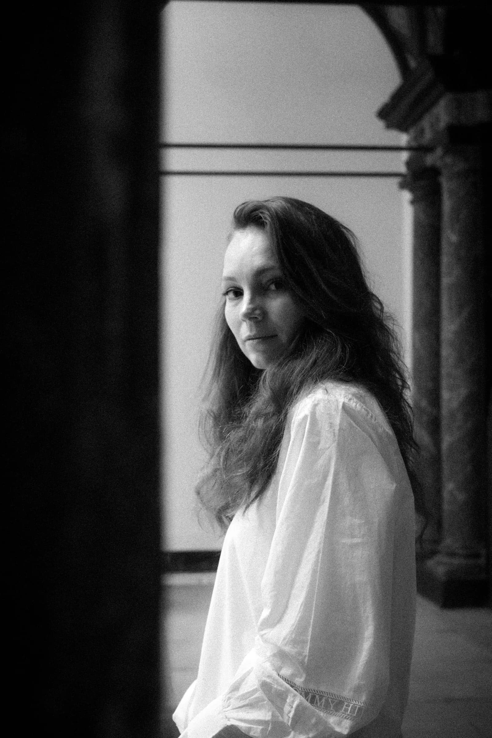 Black and white portrait between marble columns, hair loose over a white blouse