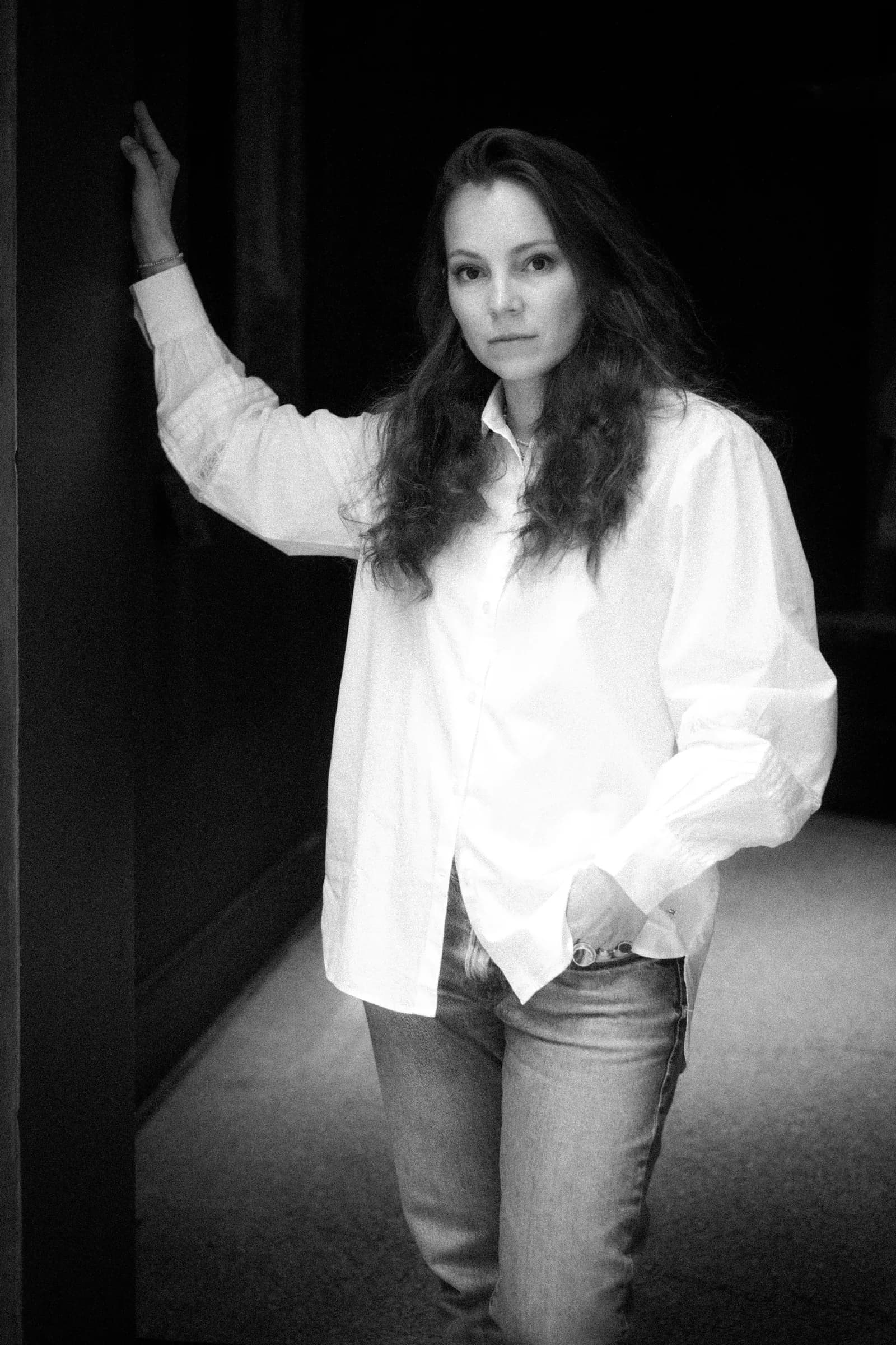 Black and white full portrait, one hand on the wall, jeans and a loose white shirt