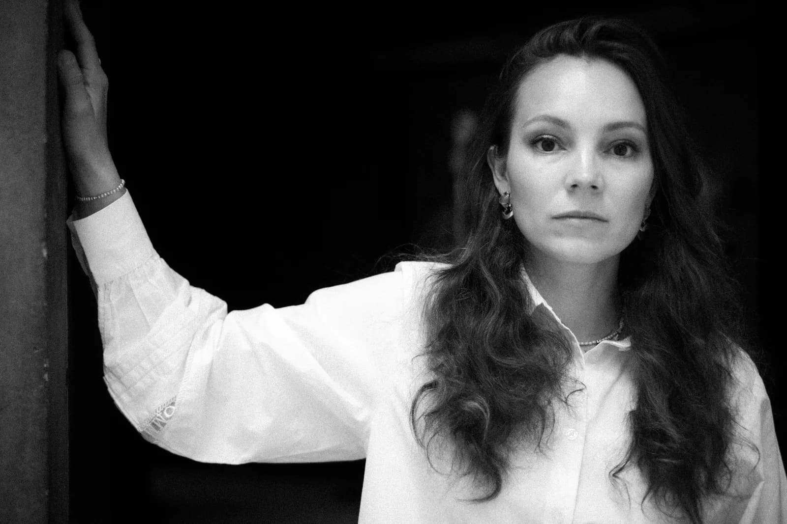 Black and white portrait of a woman in a white shirt leaning against a doorway