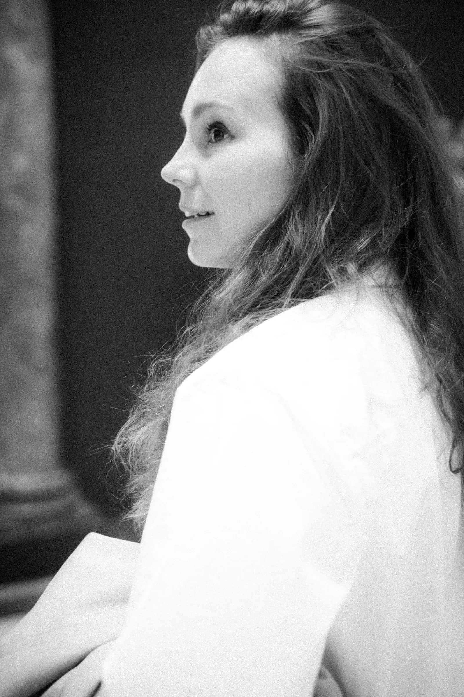 Black and white profile of a long-haired woman in a white blouse by a marble column