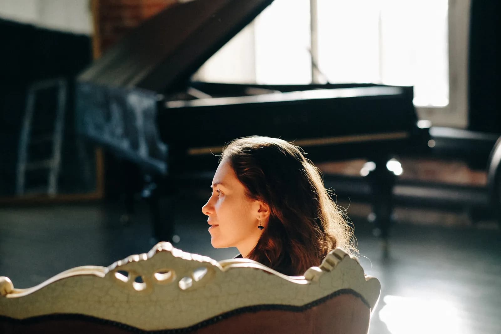 Woman looking away over a carved sofa back, a grand piano by the window behind her